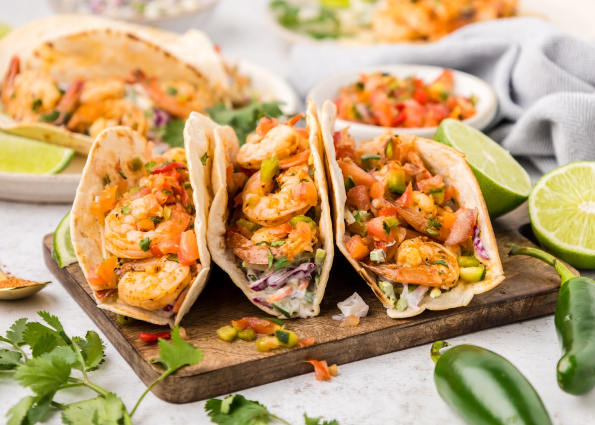 Three Cajun shrimp tacos surrounded by fresh ingredients like cilantro, lime, and jalapeños