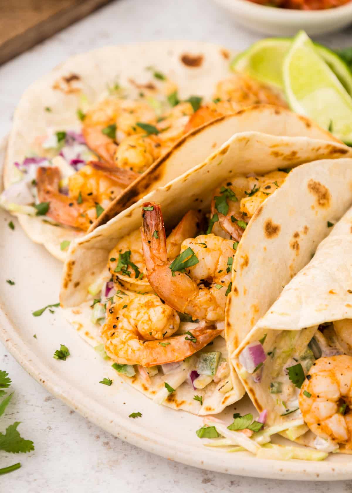 Side view of three tacos showing shrimp and creamy slaw tucked into soft tortillas