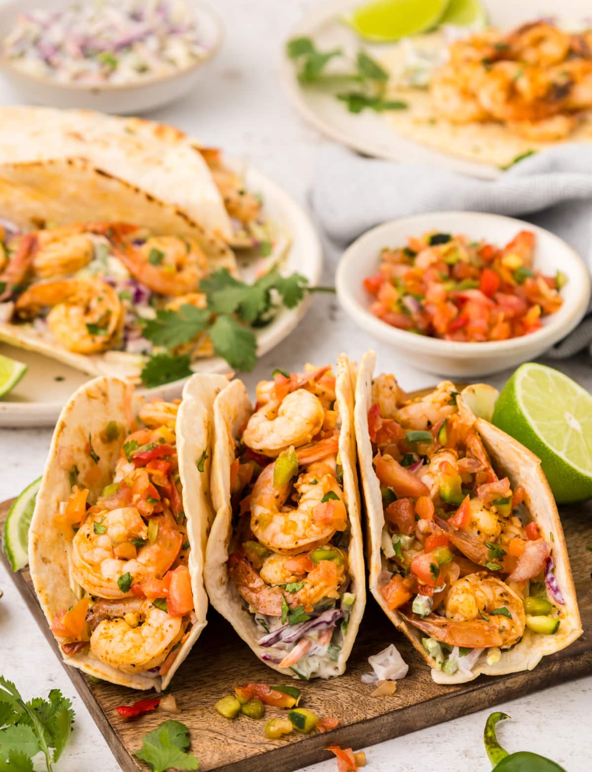 Three Cajun shrimp tacos on a cutting board with lime wedges on the side
