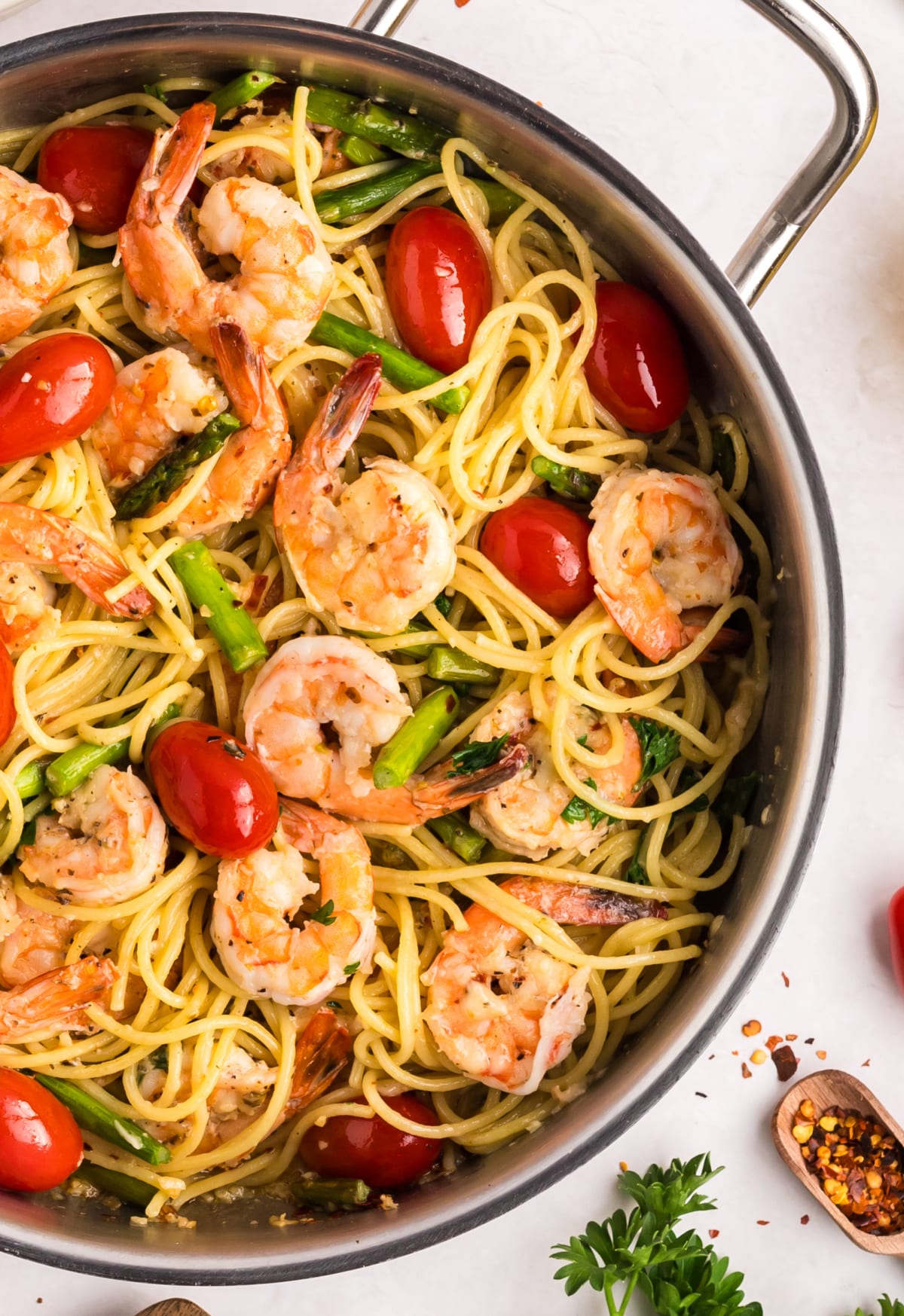 finished Garlic Shrimp Pasta with Asparagus and Tomatoes Top-down view of garlic shrimp pasta in a skillet with asparagus, cherry tomatoes, and parsley.