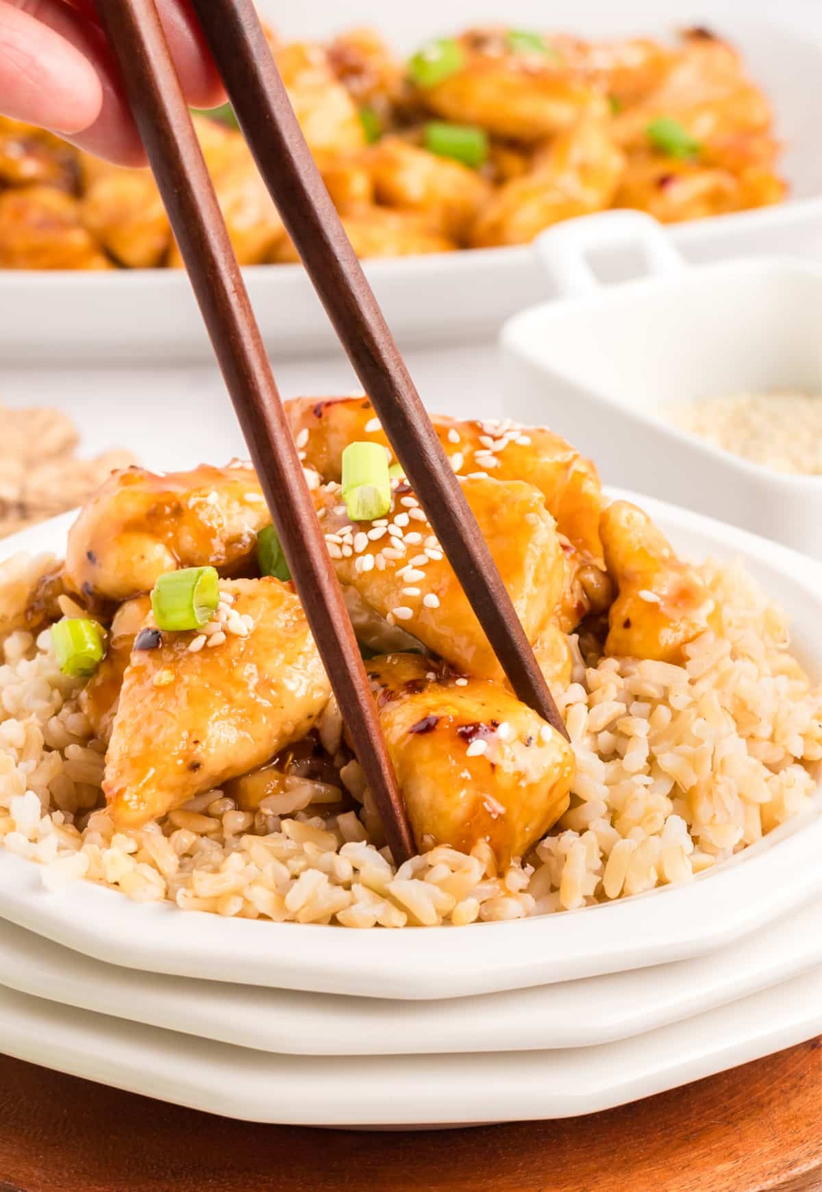 Close-up of honey sesame chicken over rice, with chopsticks lifting a bite.