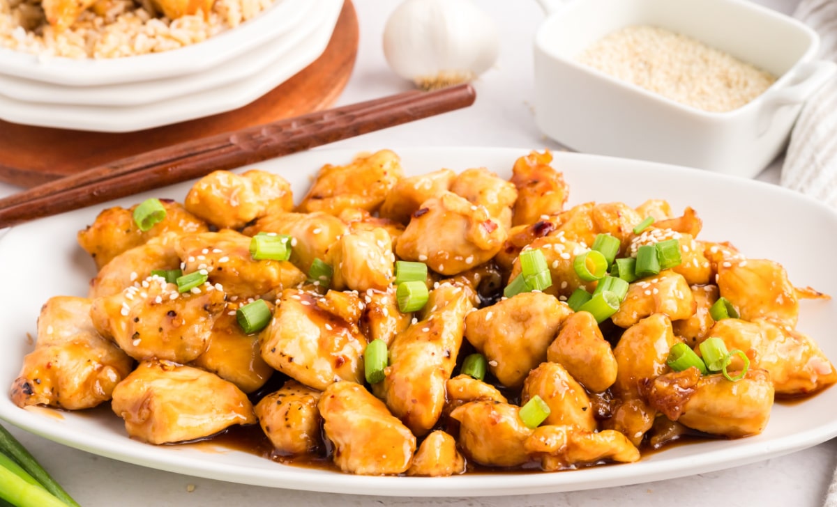 Side view of a serving platter filled with honey sesame chicken, topped with sesame seeds and green onions.