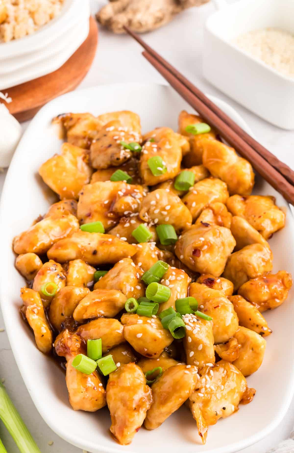 Top-down view of honey sesame chicken on a white platter, garnished with sliced green onions.