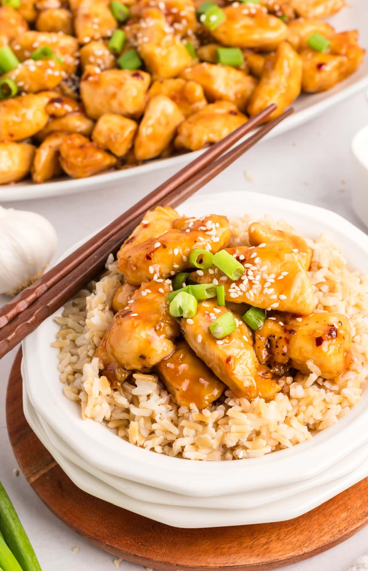 Honey sesame chicken served over white rice on a white plate, with chopsticks resting beside the dish.