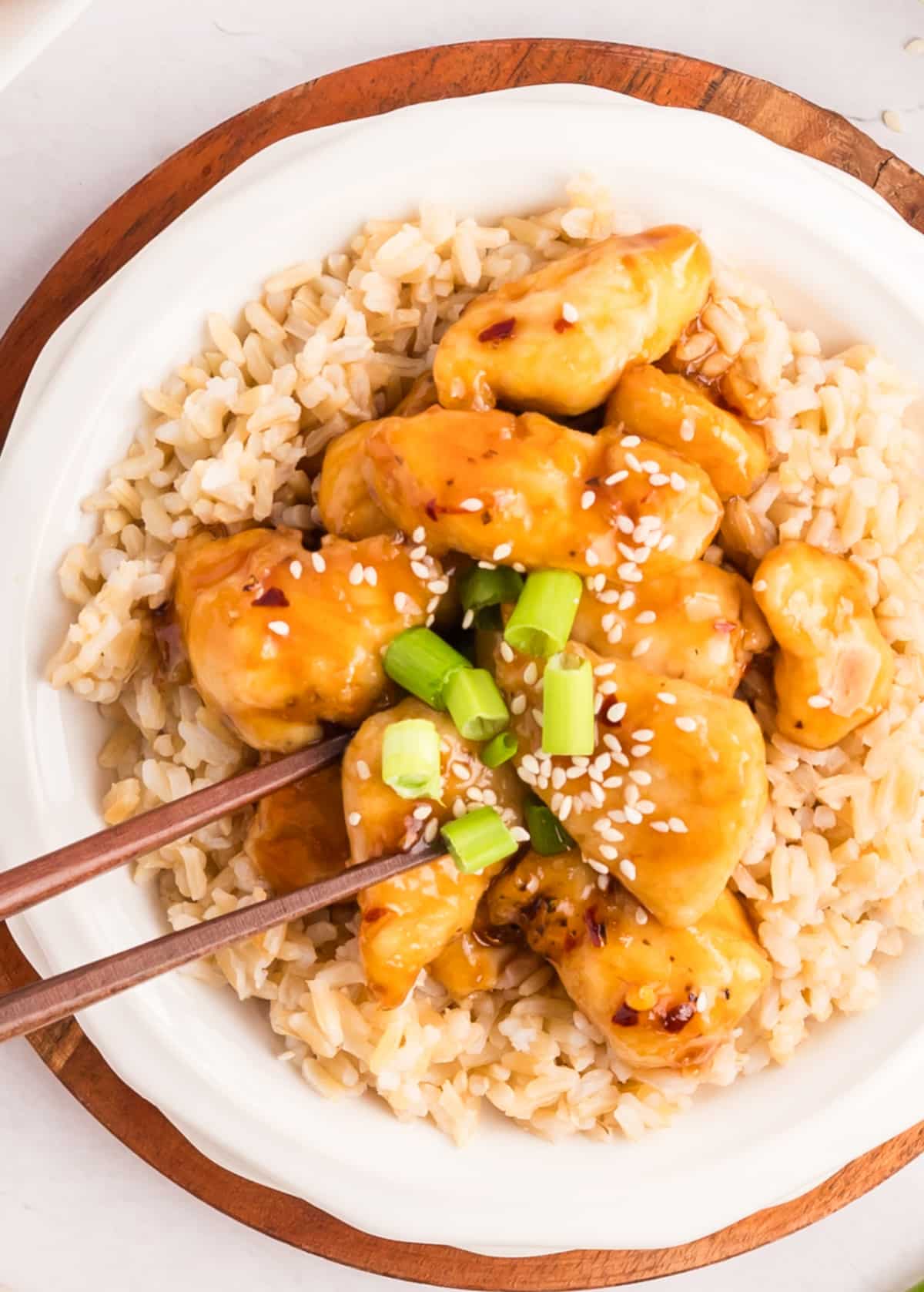 Overhead shot of a single serving of honey sesame chicken on a plate, with sauce and garnishes visible.