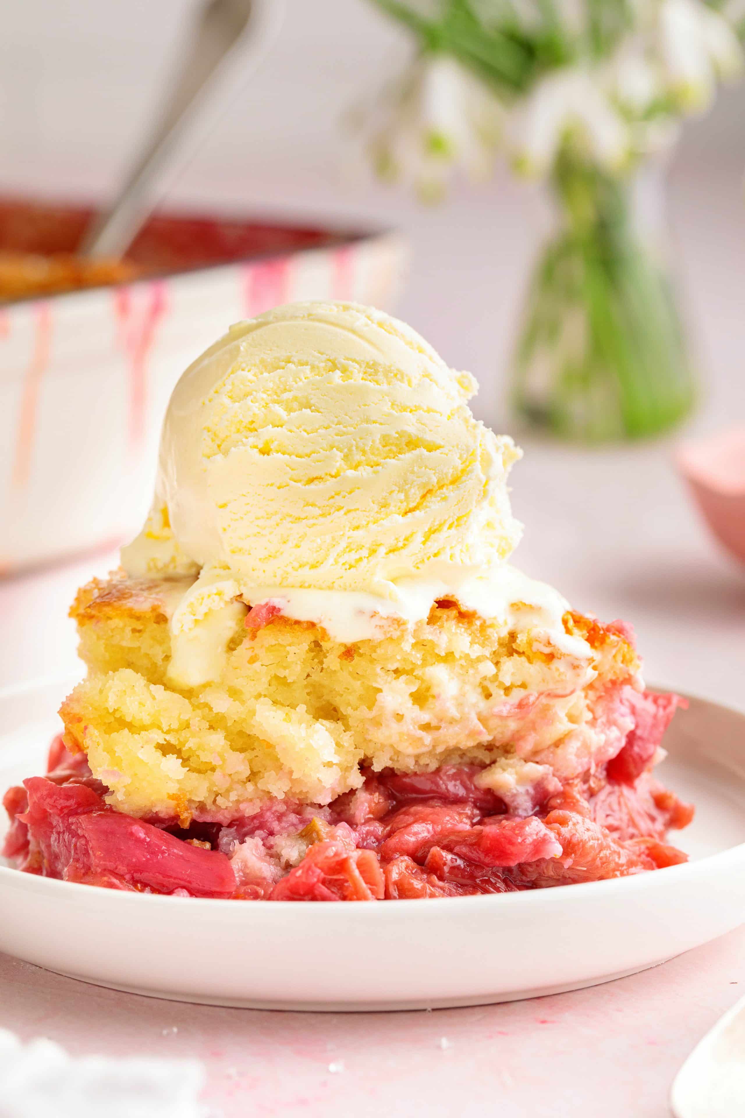 A plated serving of rhubarb cobbler topped with a scoop of melting vanilla ice cream.