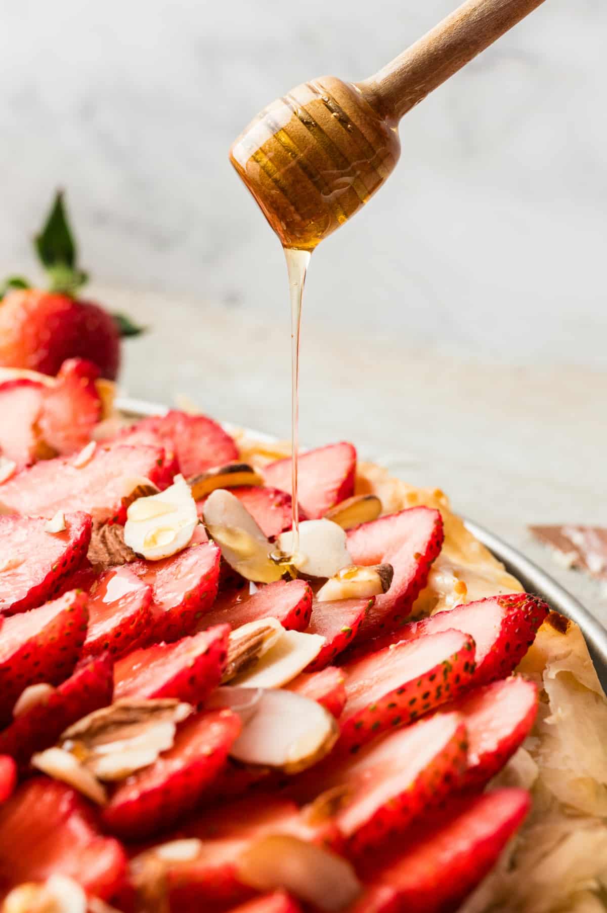 Strawberry Goat Cheese Tart (phyllo dough) with drizzling honey Close-up of a honey wand drizzling honey over a slice of the strawberry goat cheese tart.