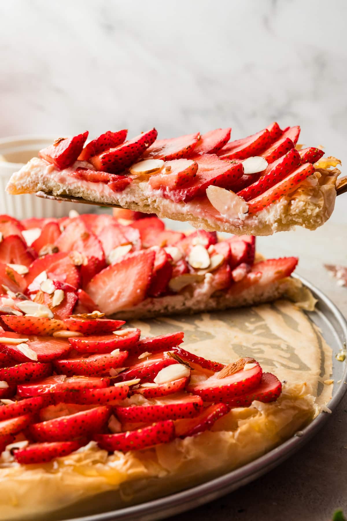 Strawberry Goat Cheese Tart (phyllo dough) being sliced Side view of a slice being lifted from the tart, showing the flaky phyllo crust and creamy goat cheese layer.