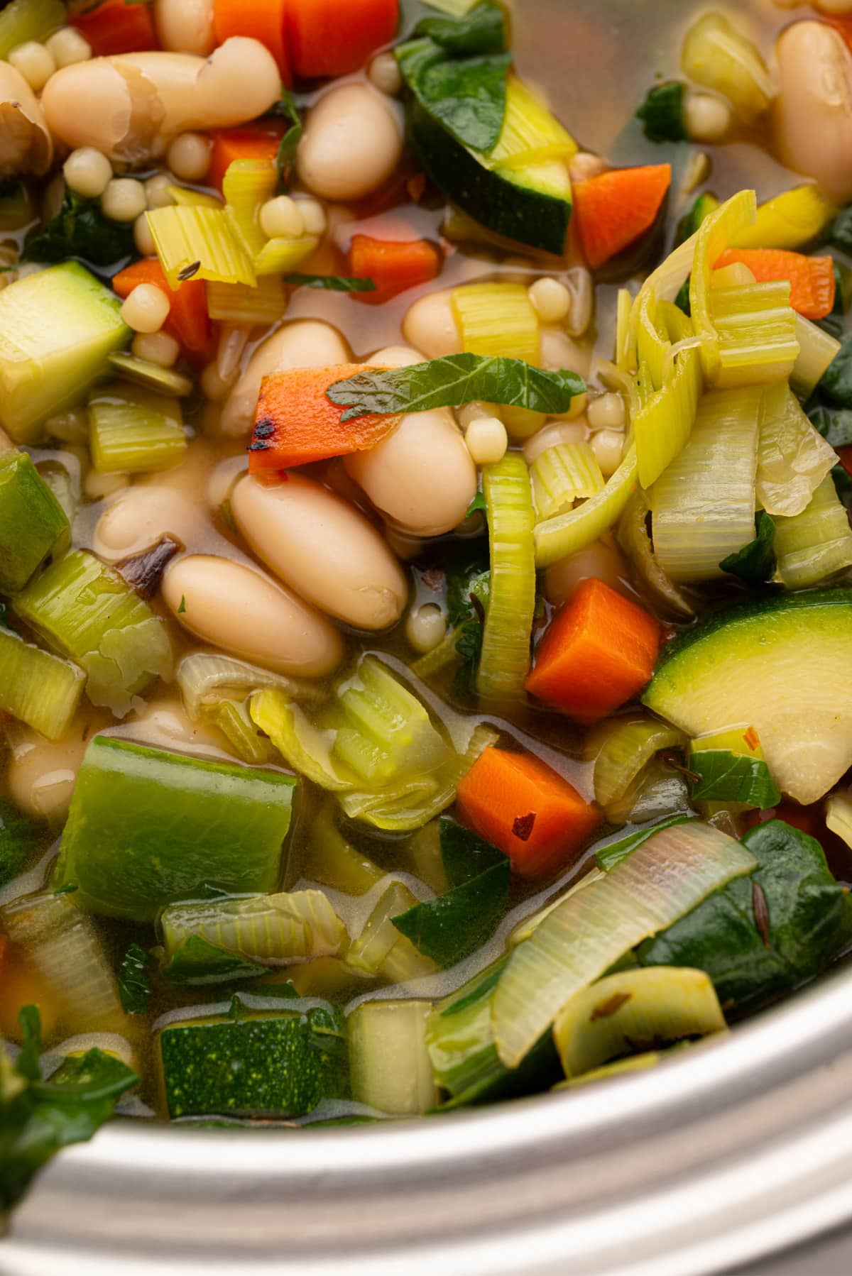 Close-up of cooked green minestrone in the pot Close-up of green minestrone simmering in the pot with pasta pearls, beans, and fresh herbs