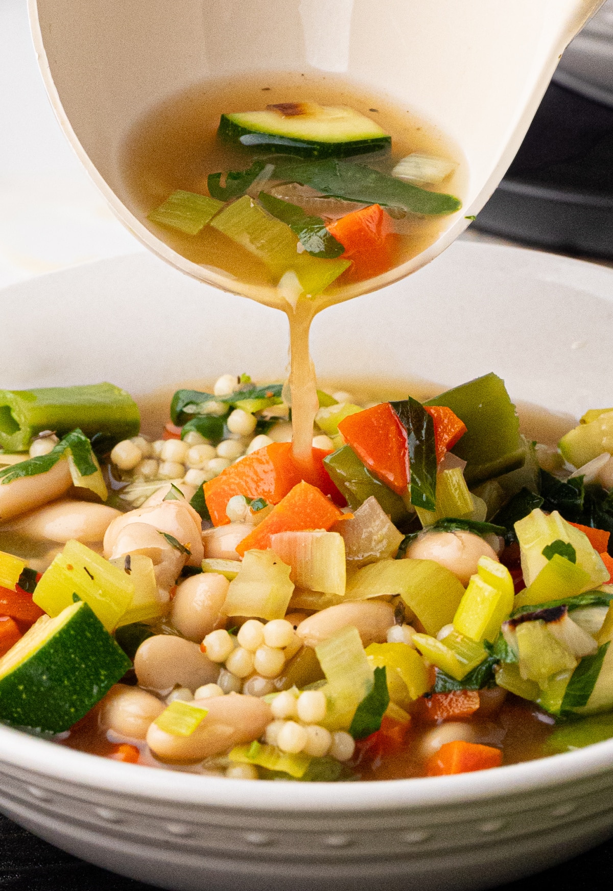 Ladle pouring green minestrone into serving bowl Green minestrone being poured from a ladle into a white bowl