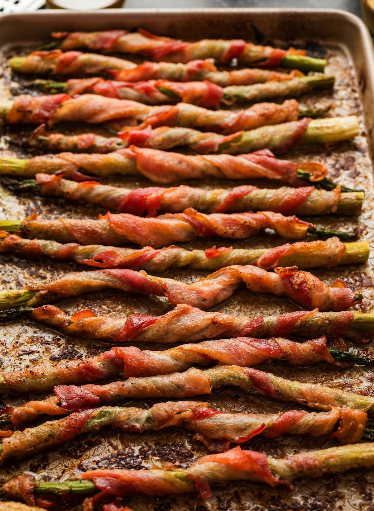 Finished bacon-wrapped asparagus on baking sheet from above Full baking sheet with rows of roasted bacon-wrapped asparagus