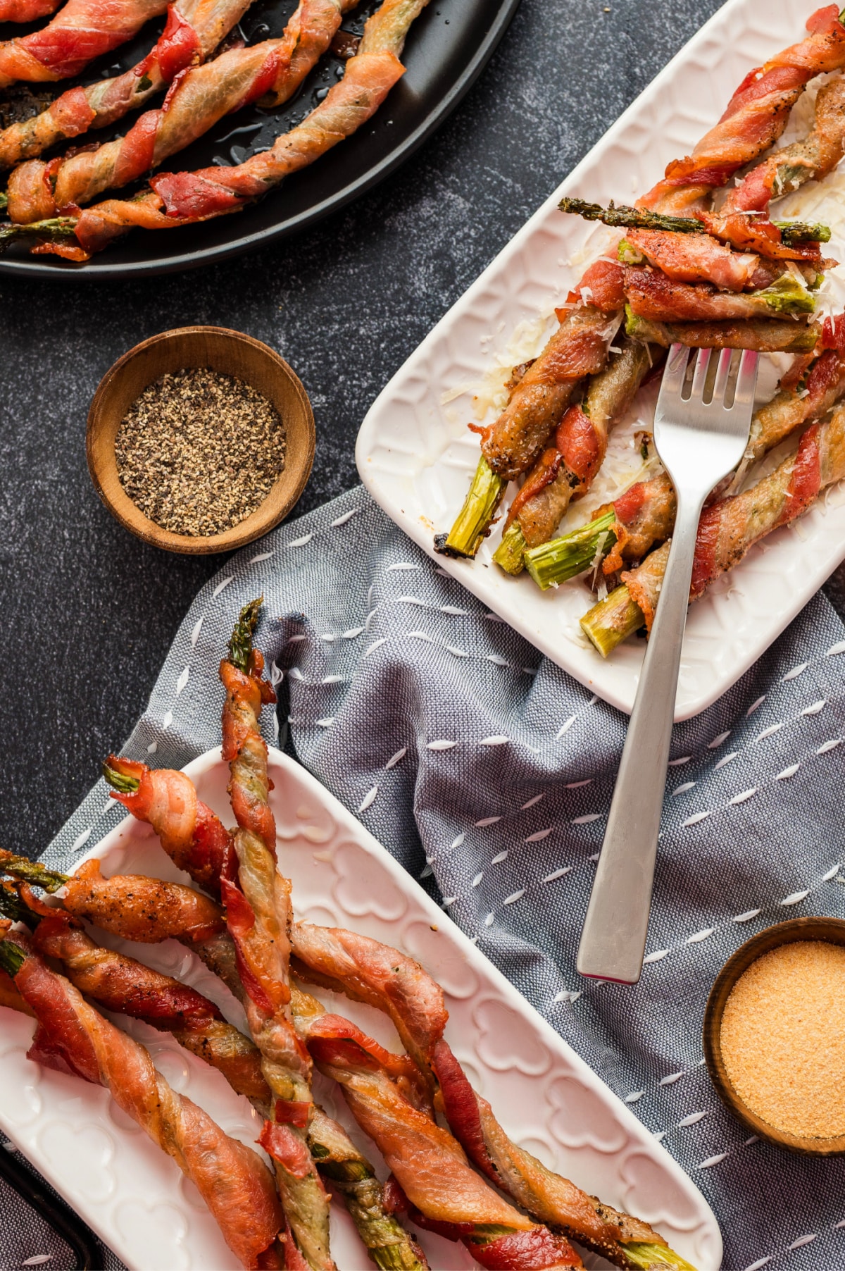 Fork with a bite of bacon-wrapped asparagus on serving plates Overhead shot of two serving plates with bacon-wrapped asparagus and a fork holding a bite