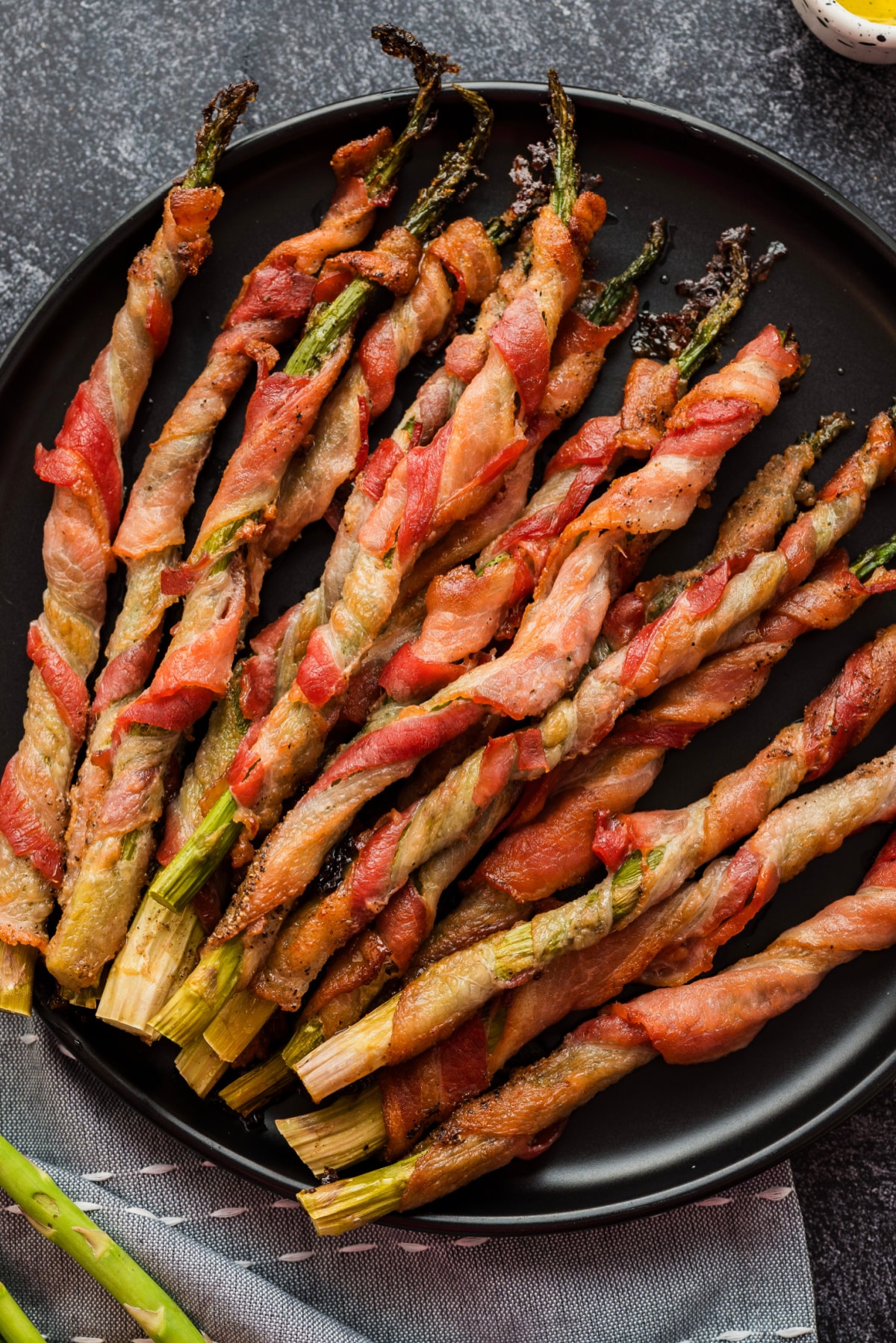 Bacon-wrapped asparagus served on black plate from above Overhead shot of roasted bacon-wrapped asparagus served on a black plate