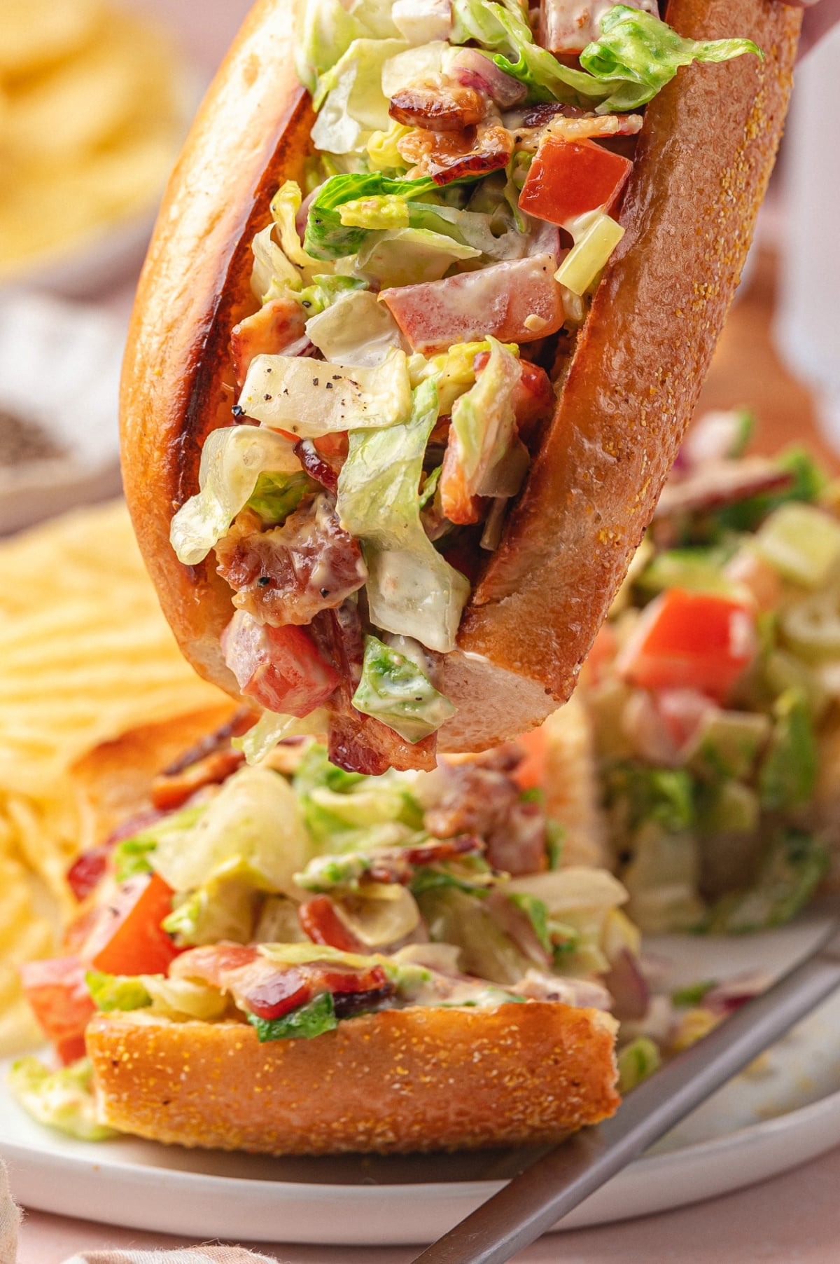 Chopped BLT hoagie sandwich close-up with others behind Close-up of a chopped BLT hoagie filled with creamy bacon lettuce tomato filling, with more hoagies blurred in the background.
