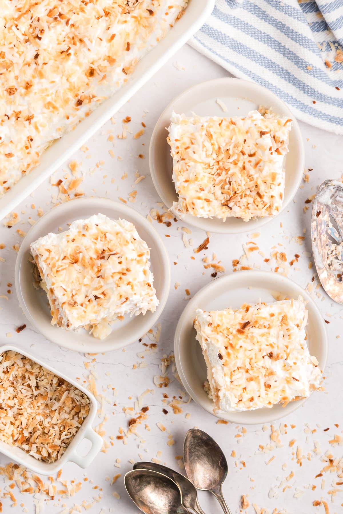 Overhead shot of three slices of coconut poke cake served on individual plates.