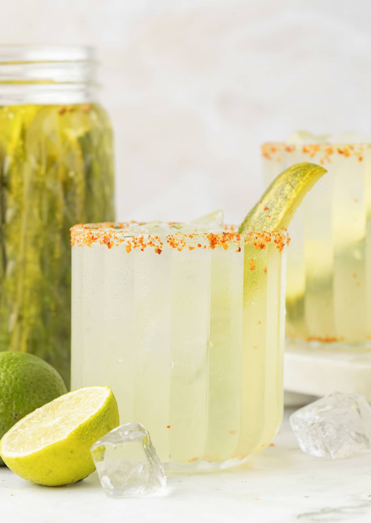 Margarita cocktail with a jar of dill pickles and fresh limes in the background
