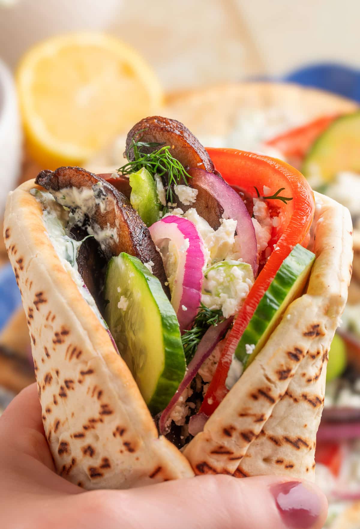 Hand holding a finished portobello mushroom gyro, ready to eat. 