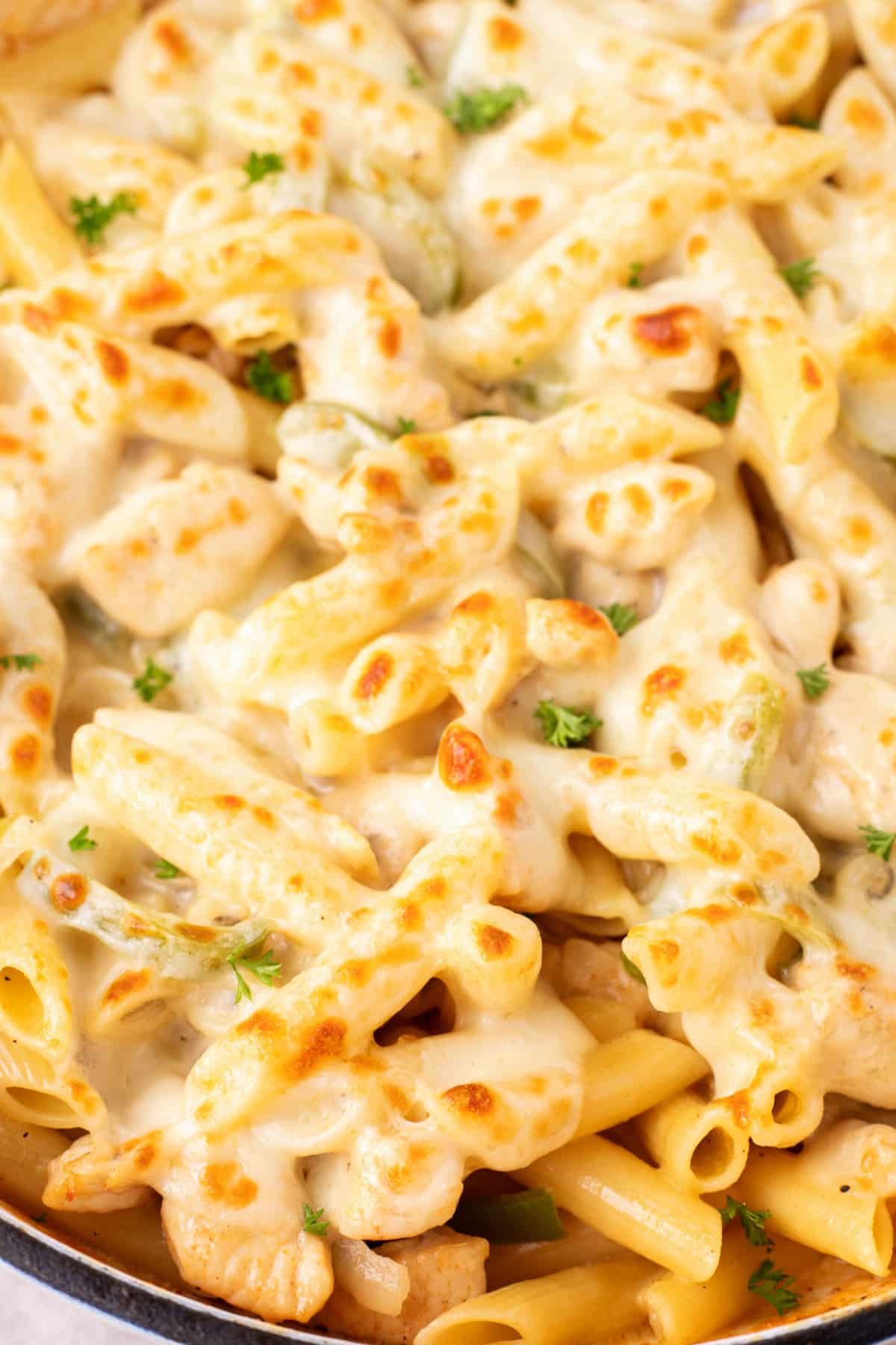 Close-up of cheesy chicken Philly cheesesteak pasta in a skillet Close-up of baked chicken Philly cheesesteak pasta with golden melted provolone and parsley