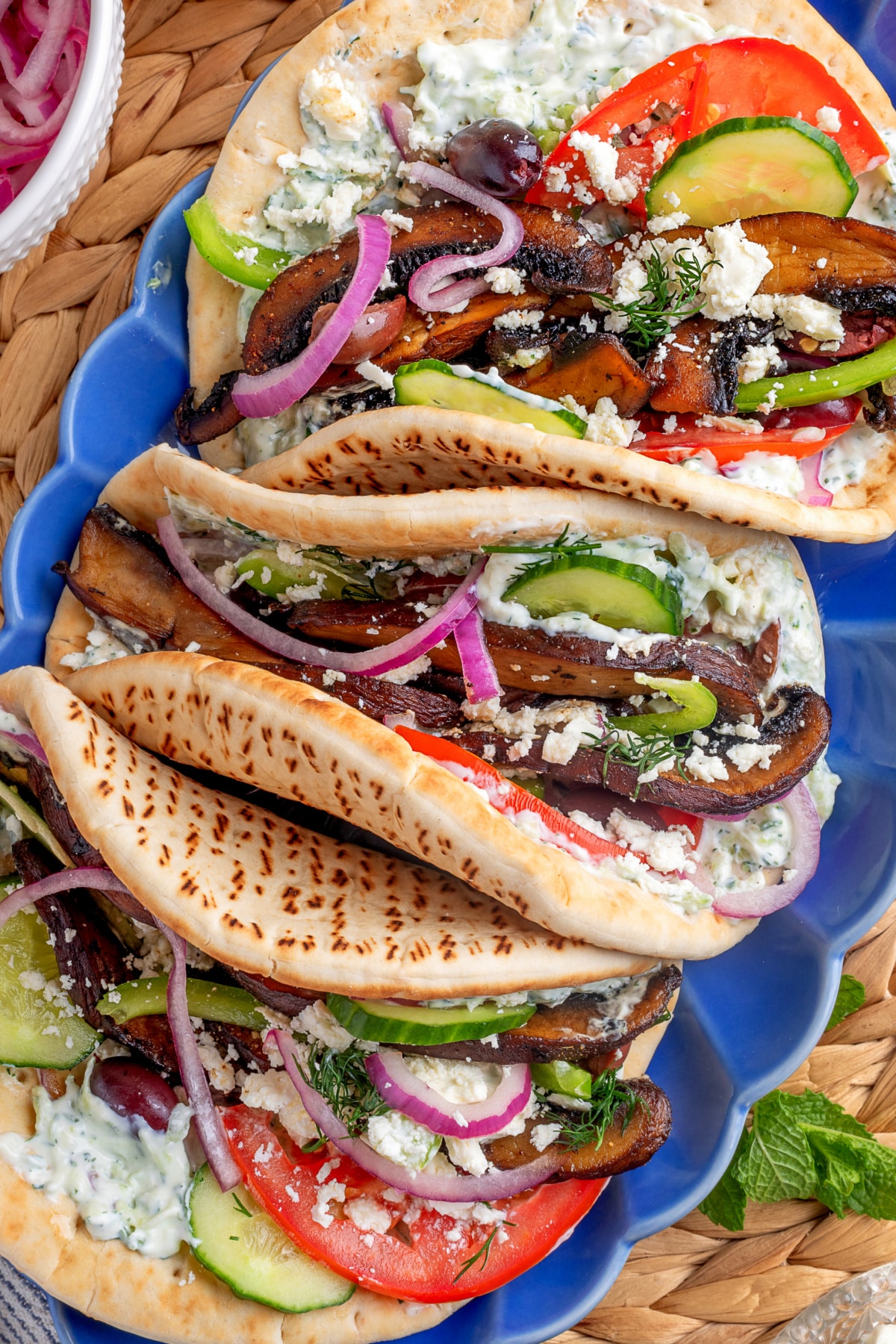 Overhead shot of finished gyros topped with vegetables and tzatziki on a blue platter. 