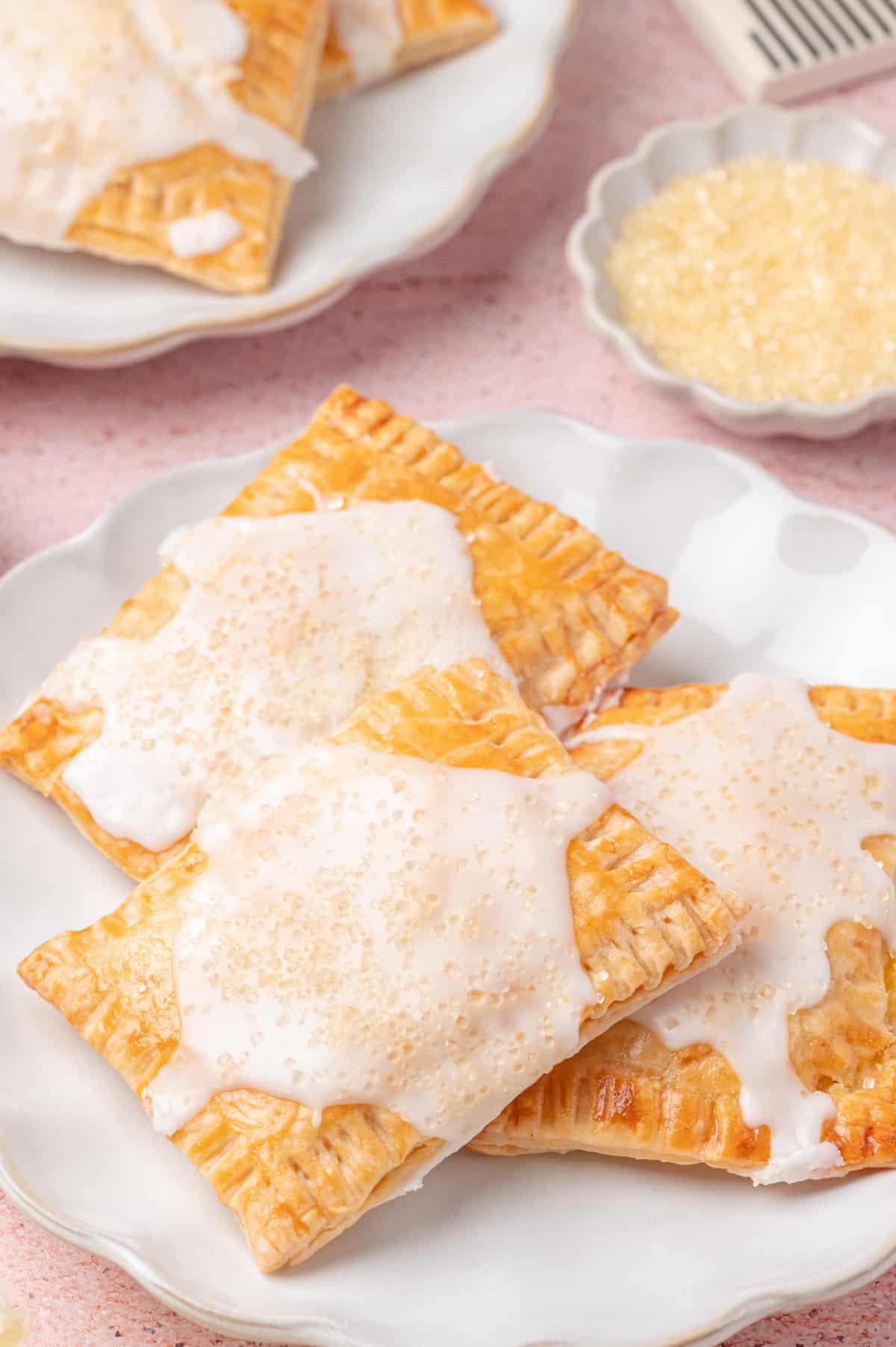 Homemade lemon pop tarts made from pie crust Close-up of glazed lemon pop tarts stacked on a white plate with coarse sugar on top