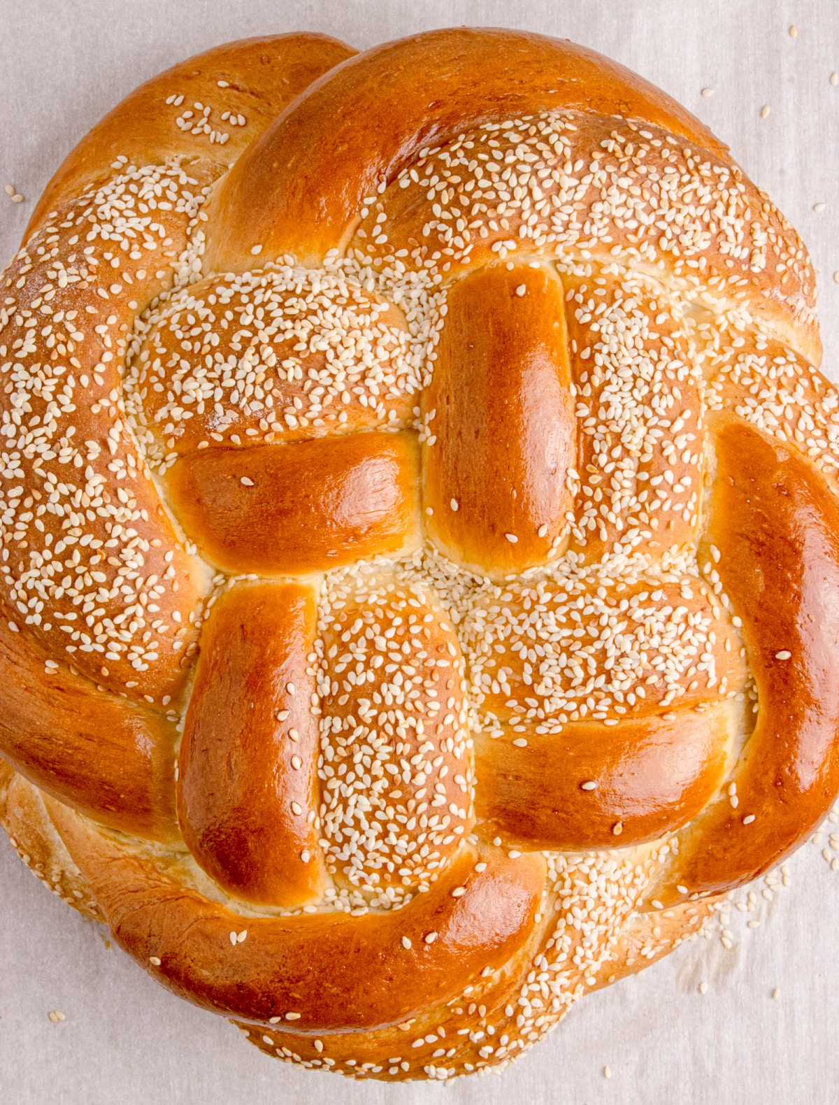 Golden brown braided round challah bread topped with sesame Baked sesame seed round challah on parchment-lined baking sheet