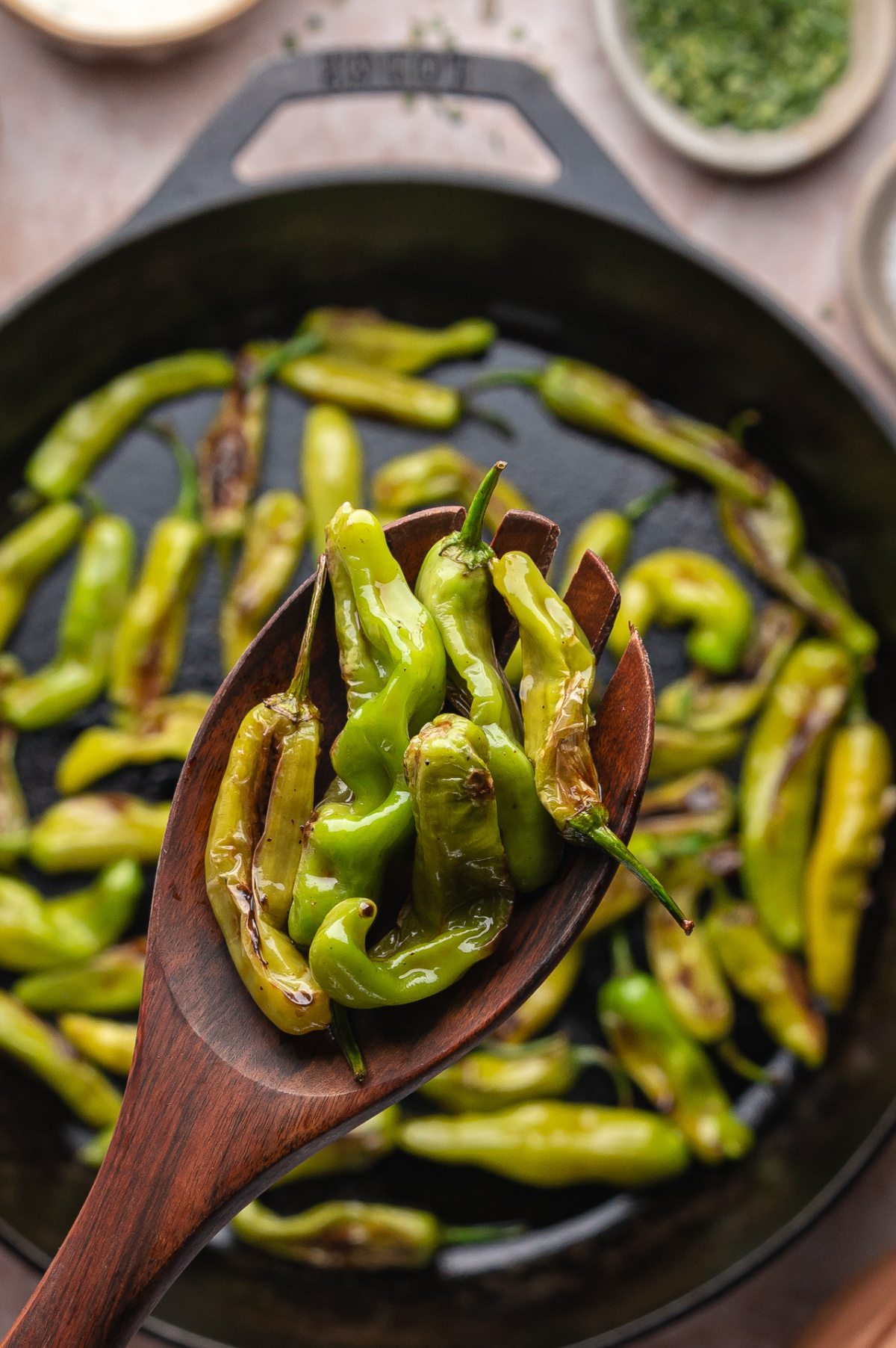 Close-up of blistered peppers on a wooden spoon held over a cast iron pan