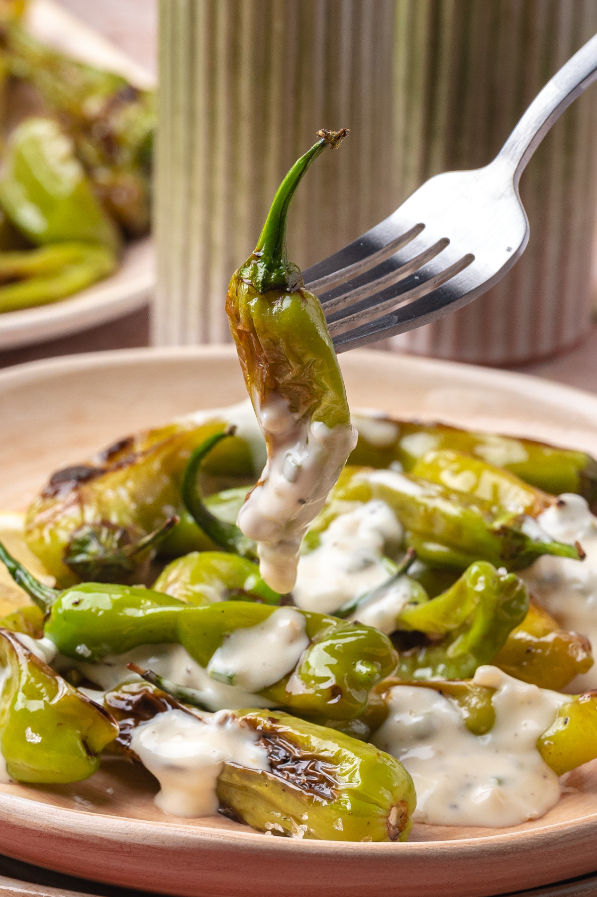 Fork lifting a blistered shishito pepper covered in creamy aioli