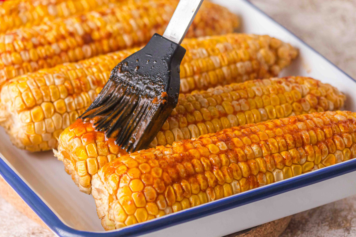 Brushing garlic butter on smoked corn on the cob with brown sugar and paprika