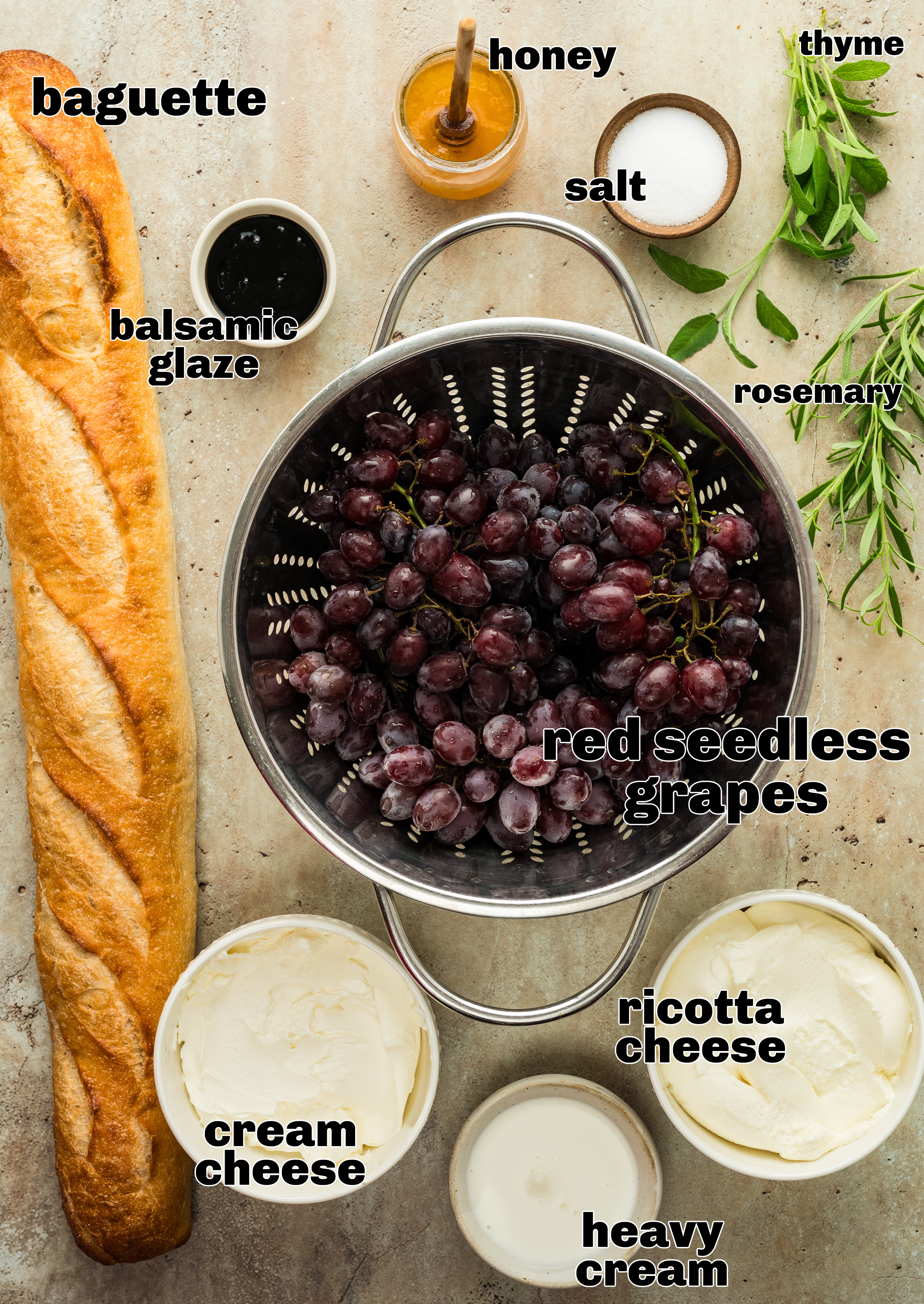 ingredients for roasted grape appetizer including ricotta, cream cheese, honey, grapes, herbs, and baguette ingredients for whipped ricotta with roasted grapes laid out on a table