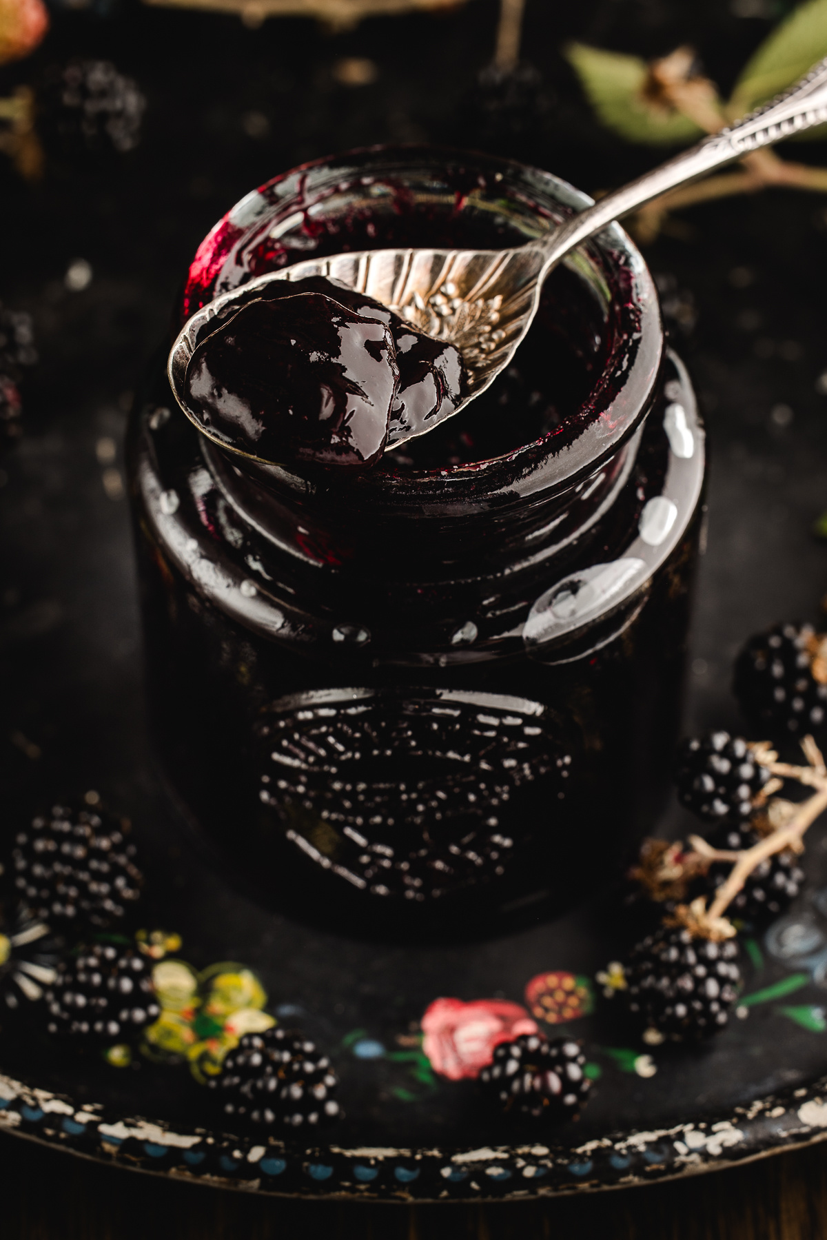 Vintage spoon dipped into a jar of glossy jam on a floral tray with berries