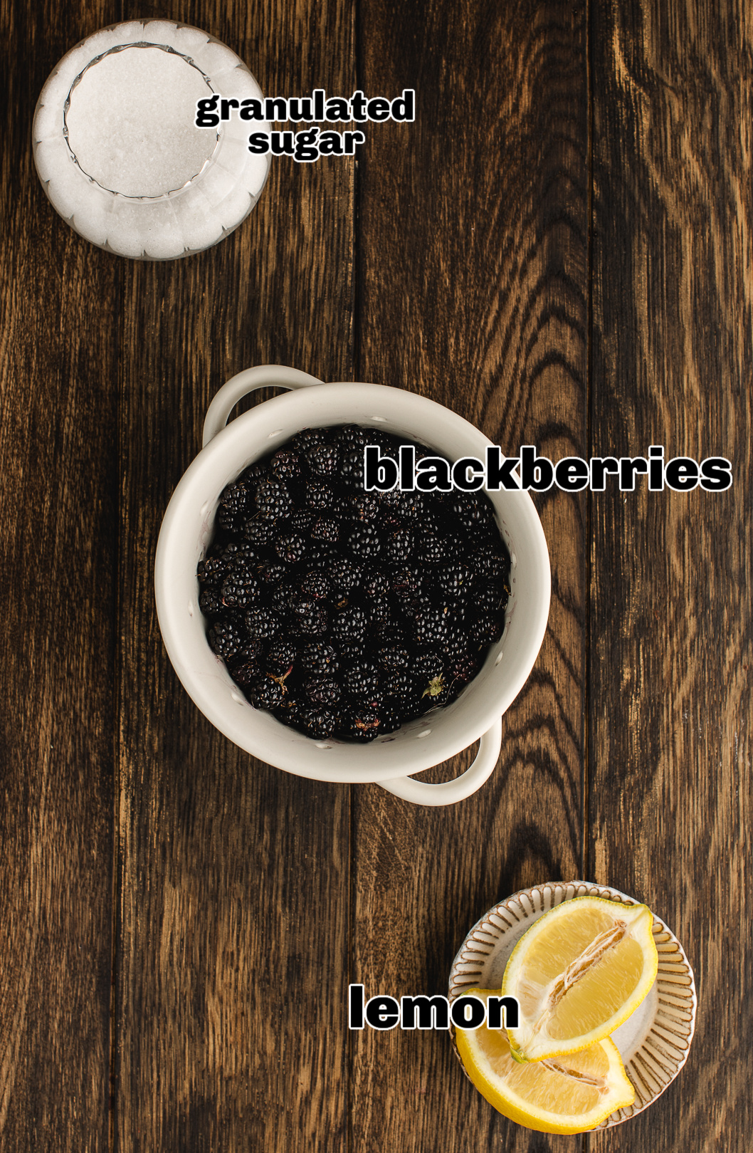 Ingredients for blackberry jam shown on wood table: fresh blackberries, sugar, and lemon