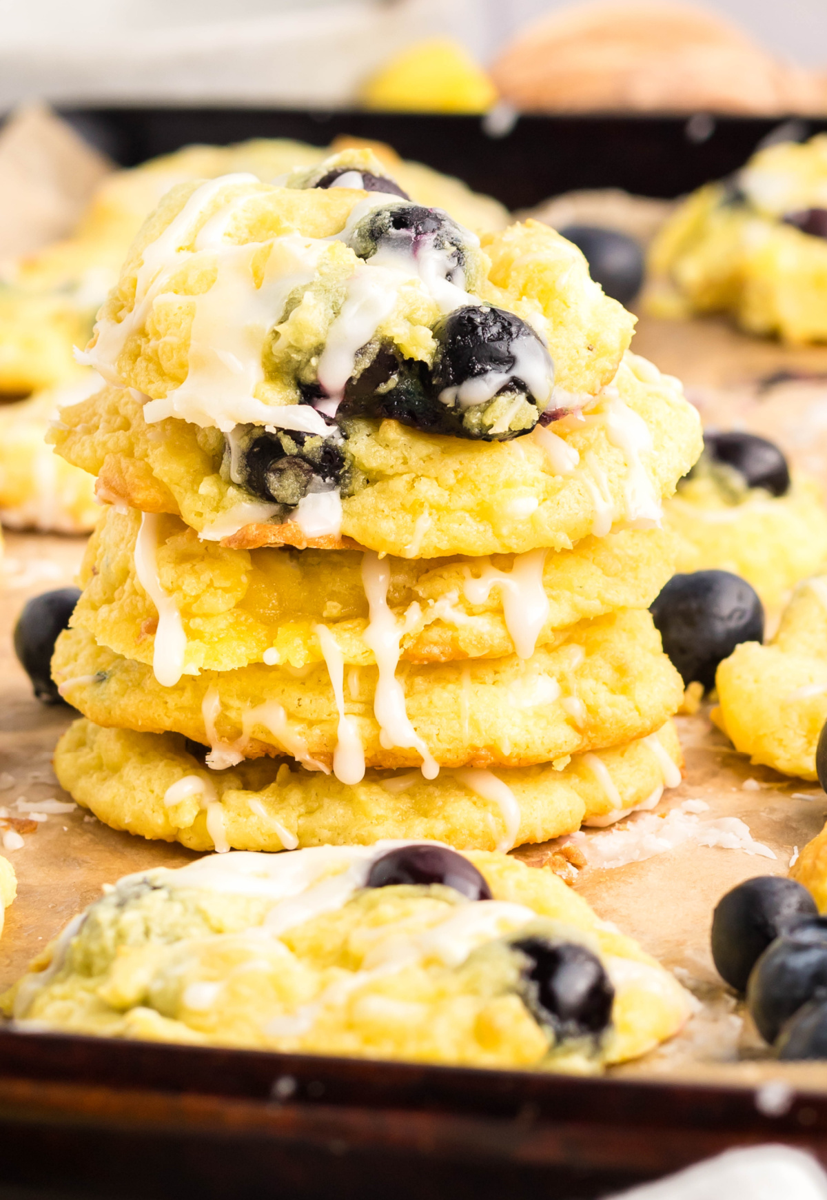 Lemon Blueberry Cookies with Glaze Drizzle Stack of soft lemon blueberry cookies with glaze and fresh blueberries on parchment