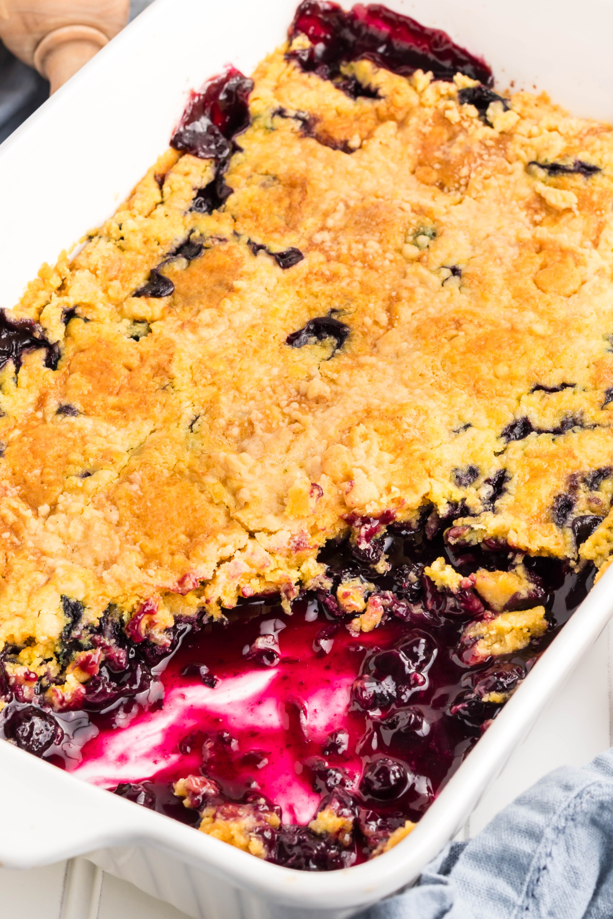 Fresh blueberry dump cake with buttery topping. Blueberry dump cake with golden crust and bubbling filling in a white dish.