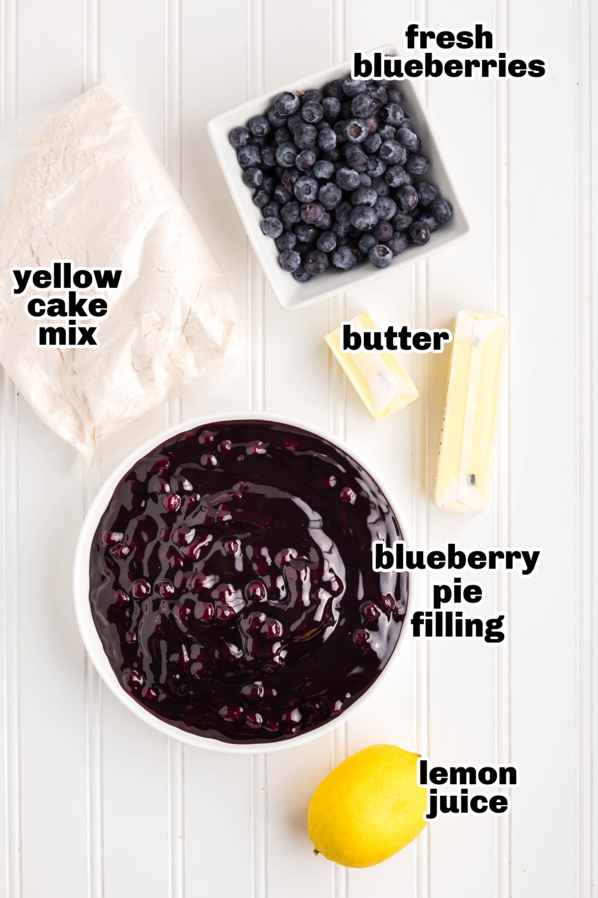 Ingredients for an easy blueberry dessert with cake mix. Overhead view of ingredients like cake mix, pie filling, blueberries, lemon, and butter on a countertop.