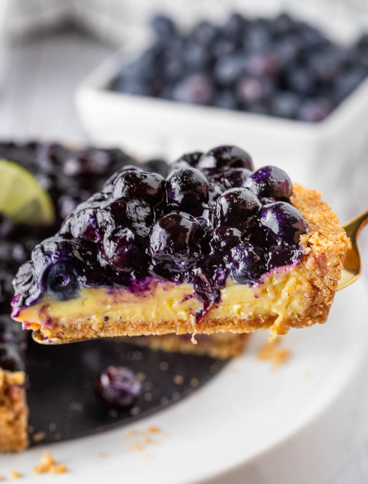Blueberry Key Lime Tart slice lifted from pan showing custard and blueberry topping.