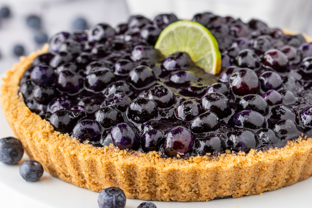 Blueberry Key Lime Tart in tart pan topped with lime wedge and fresh blueberries.