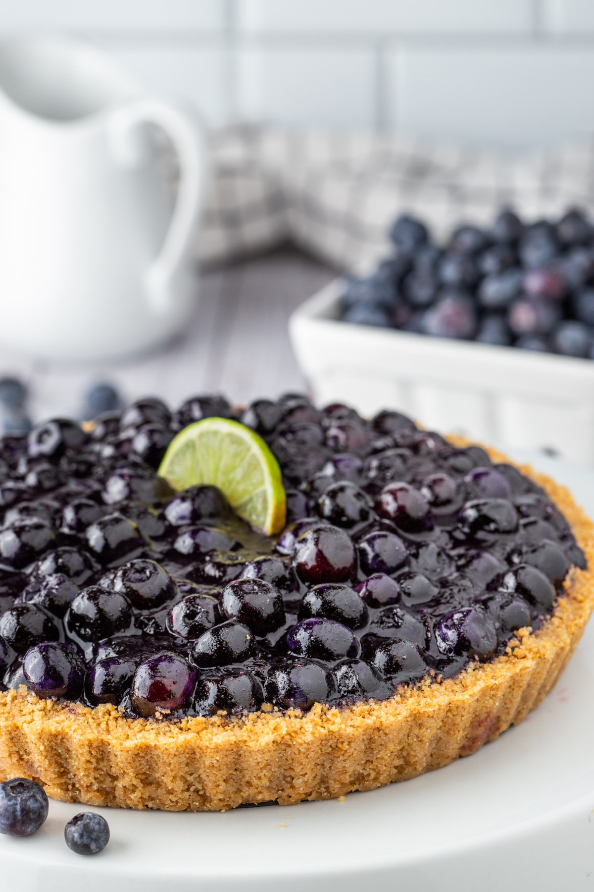 Blueberry lime tart in graham cracker crust topped with fresh blueberries and lime.