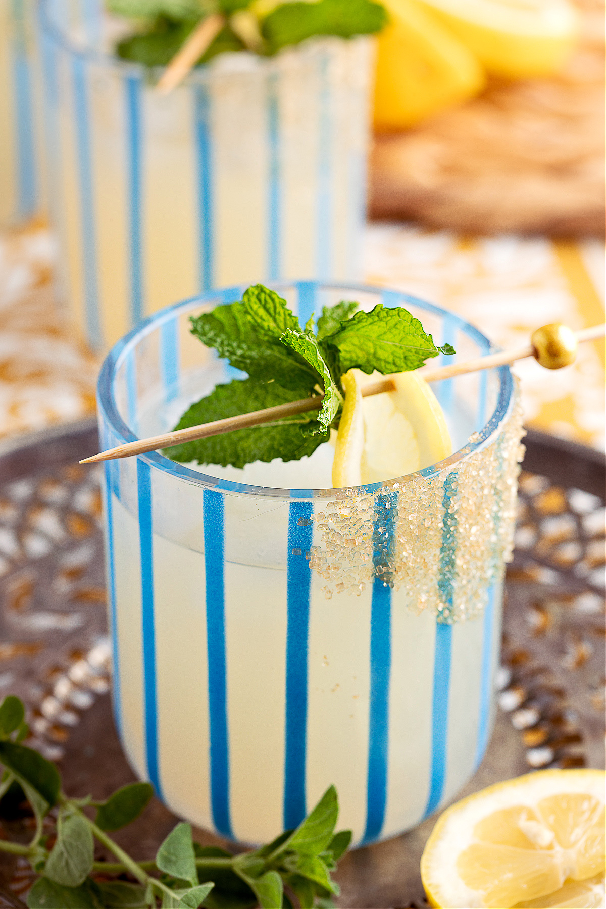 Glass of honey lemon gin smash with mint garnish, resting on a metal tray with fresh herbs and lemon slices.