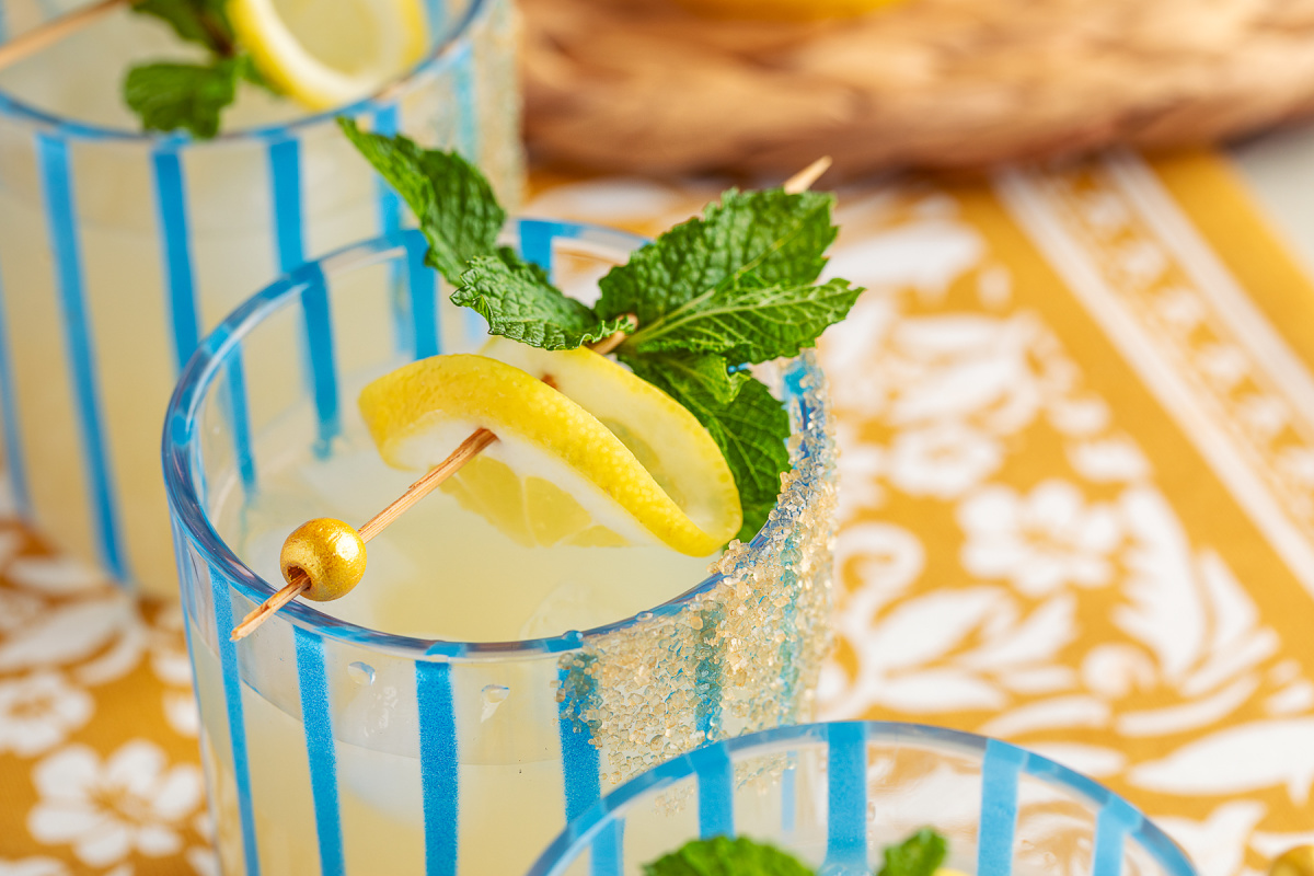 Lemon and mint gin cocktail in a rocks glass with sugar-rimmed edge, shot from an angle. 