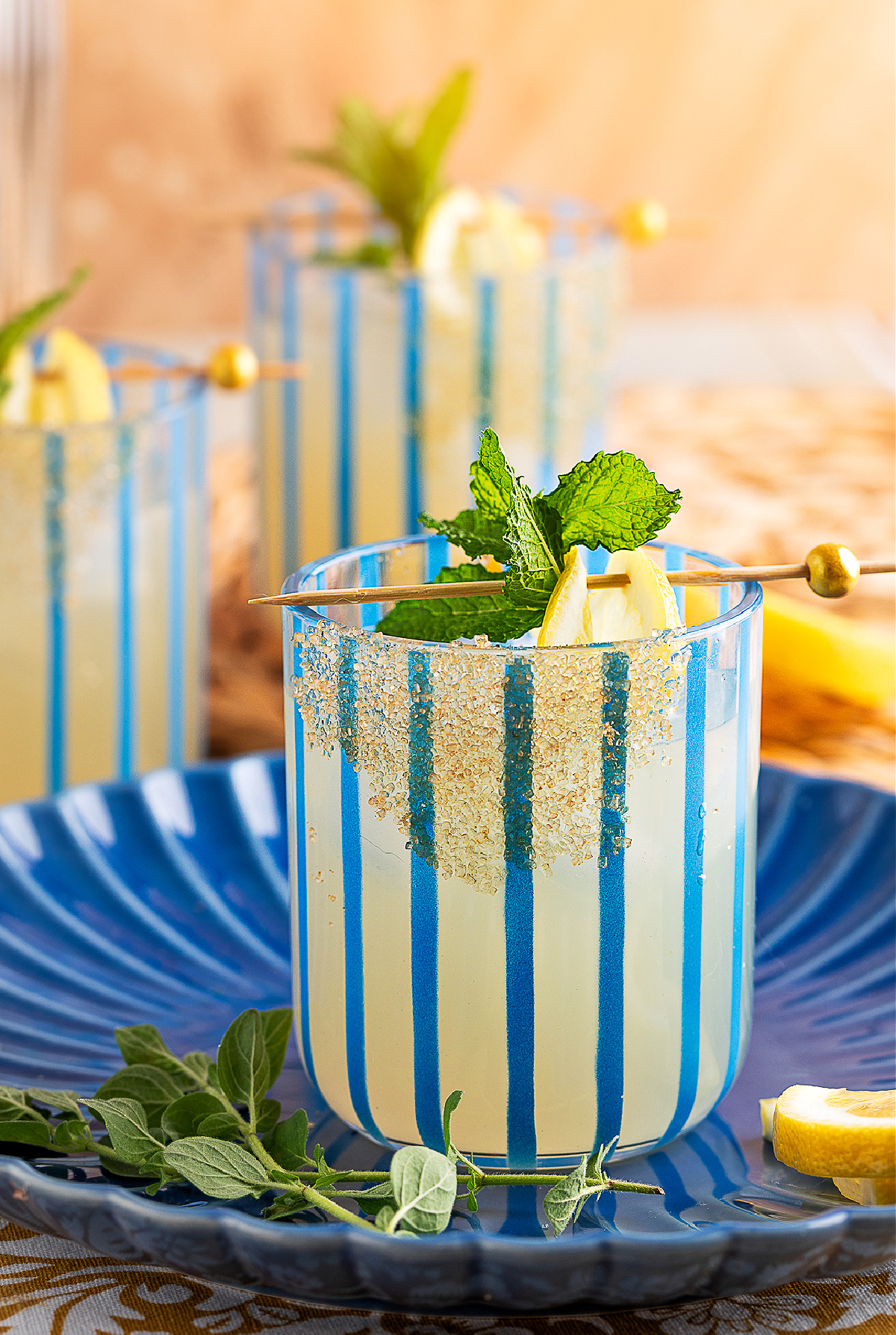 Vibrant gin smash with lemon and mint on a blue plate, surrounded by oregano and lemon wedges.