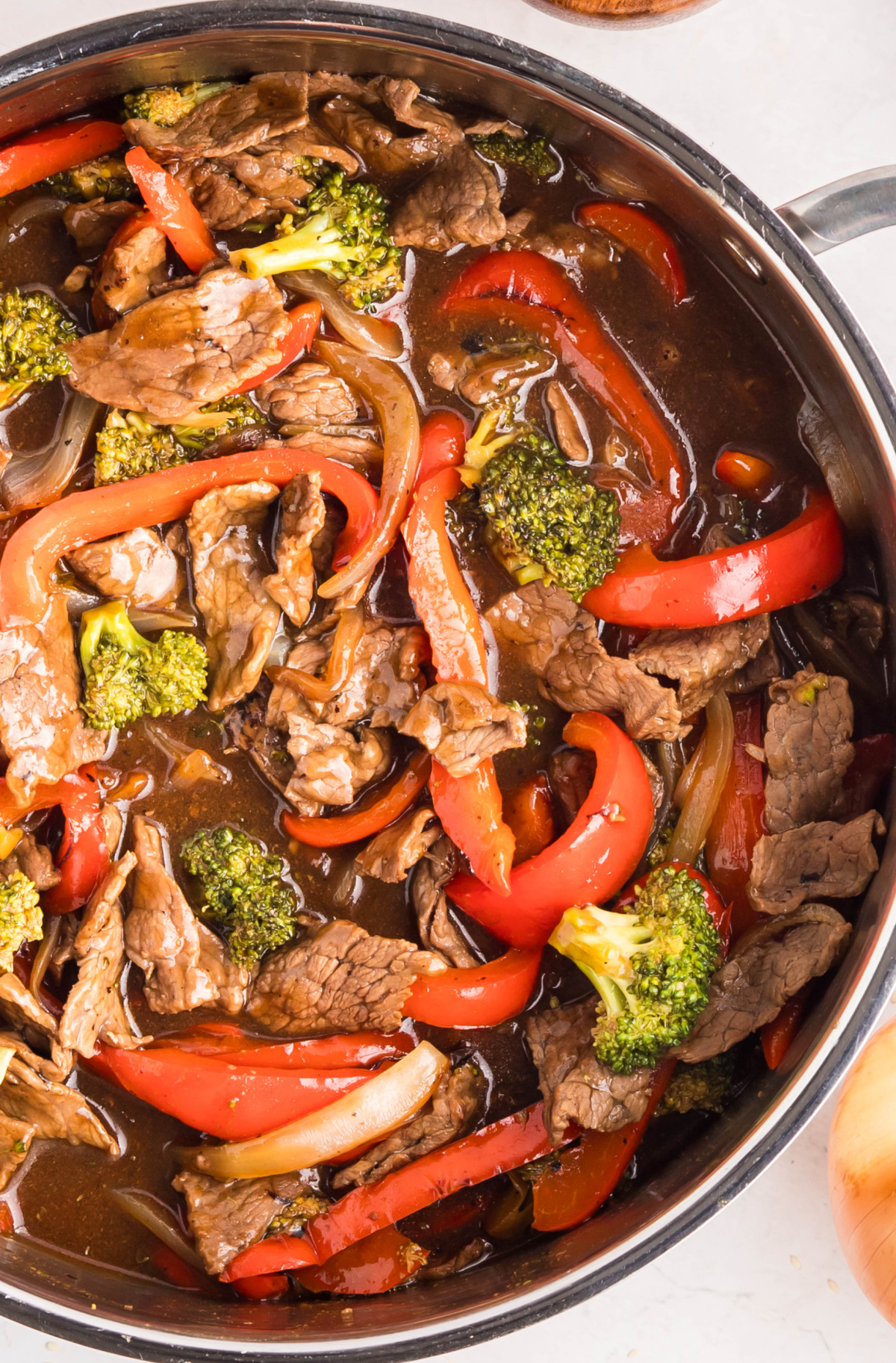 Beef, broccoli, and red peppers simmering in teriyaki sauce in a skillet