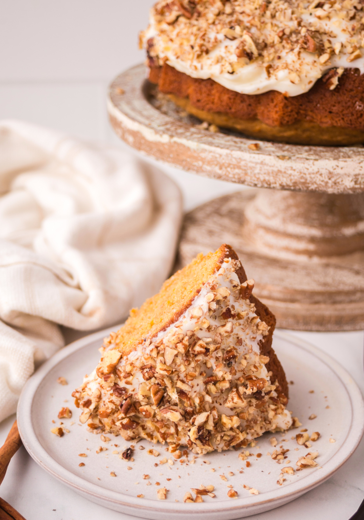 carrot bundt cake with frosting Carrot cake bundt slice covered in cream cheese frosting and walnuts on a plate.