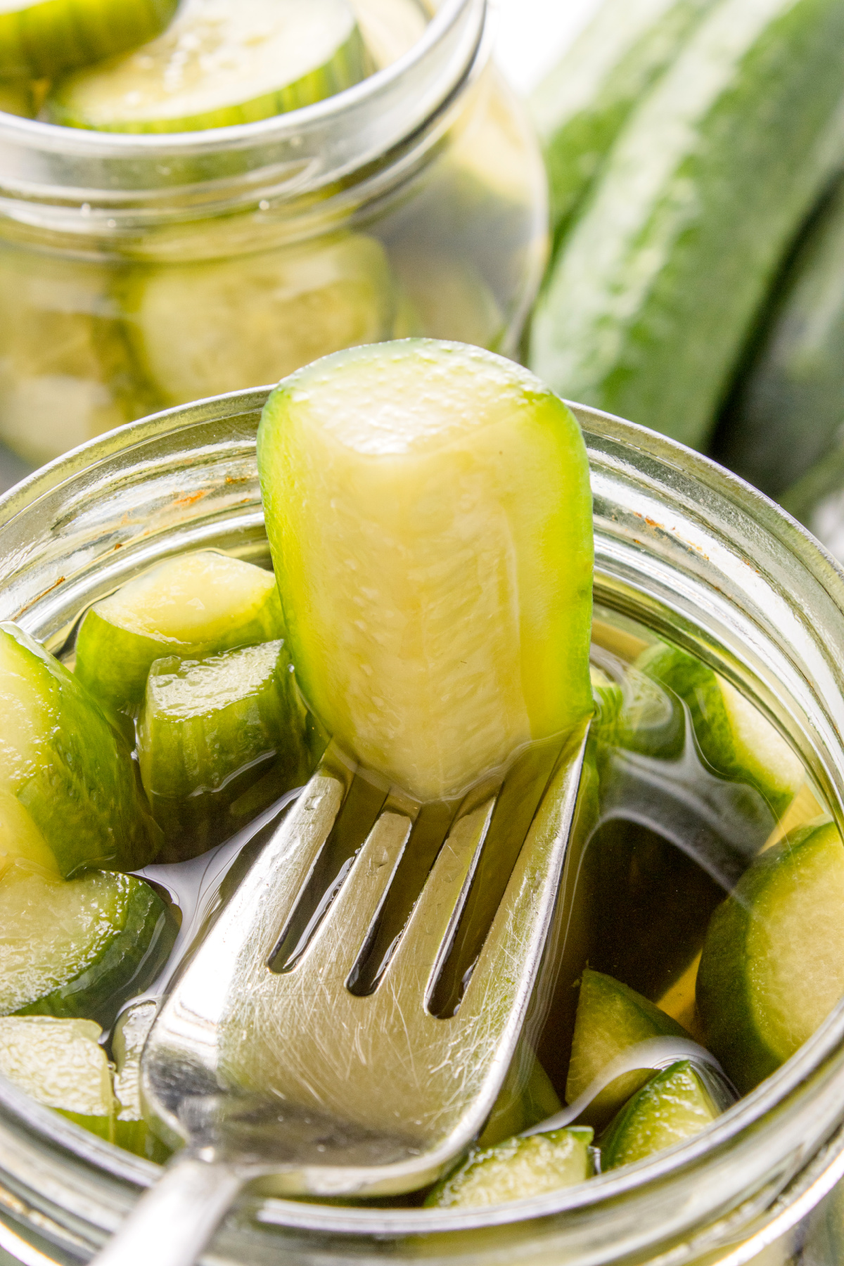 Fork lifting a crunchy slice of homemade dill pickle from the jar.