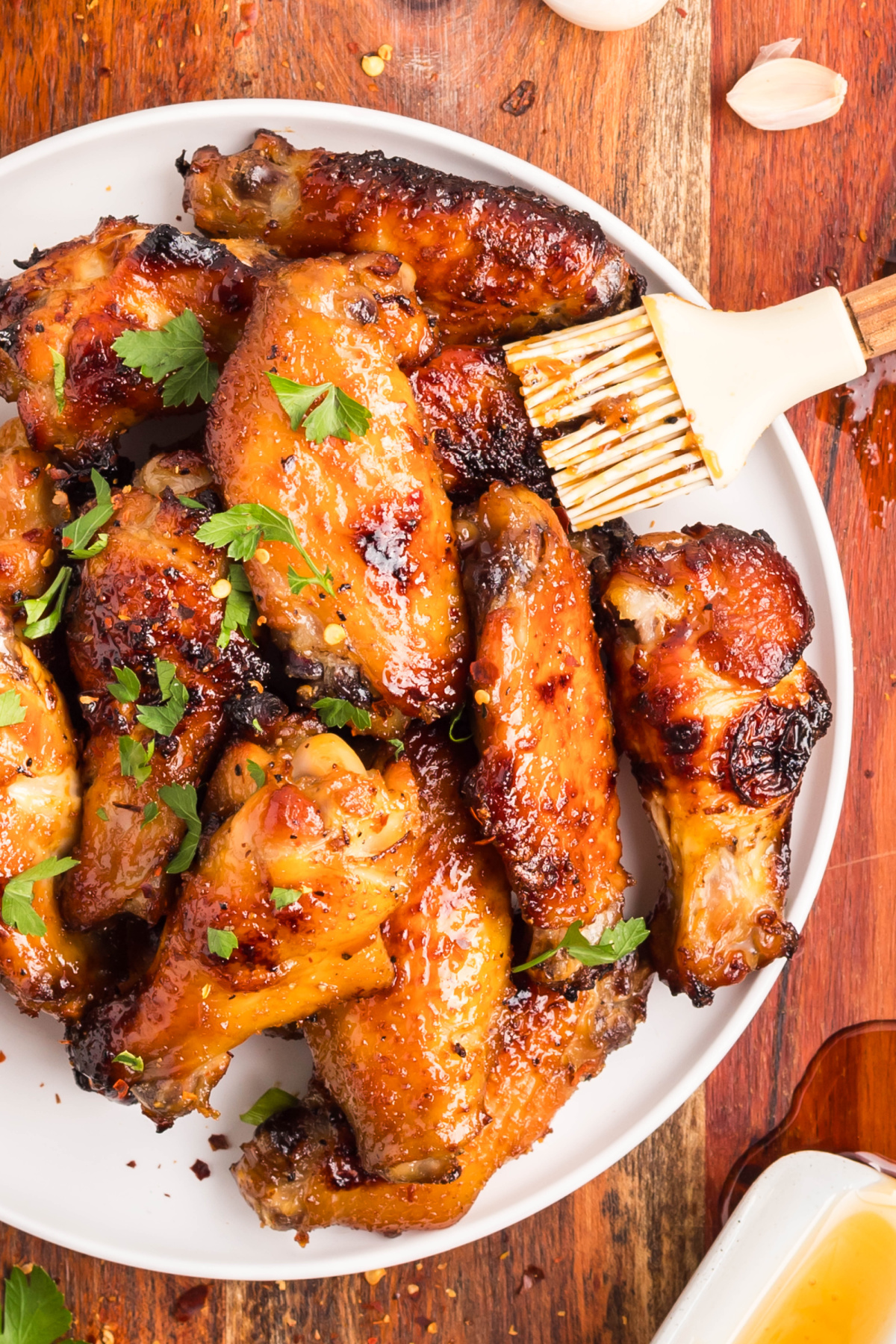 Baked honey garlic chicken wings with parsley garnish. Baked honey garlic chicken wings on a white plate with parsley and a brush of sticky sauce.