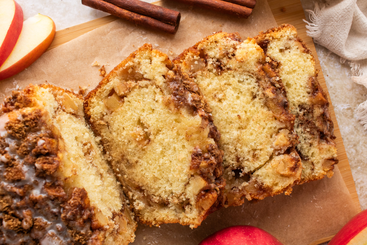 Cinnamon swirl apple bread sliced on parchment with fresh apples and cinnamon sticks.