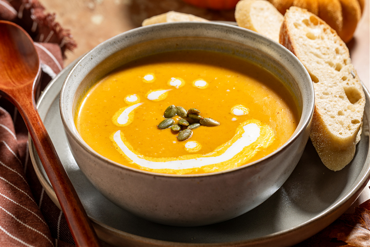 creamy pumpkin soup with bread creamy roasted garlic pumpkin soup in a gray bowl with cream swirl and pumpkin seeds, surrounded by bread slices