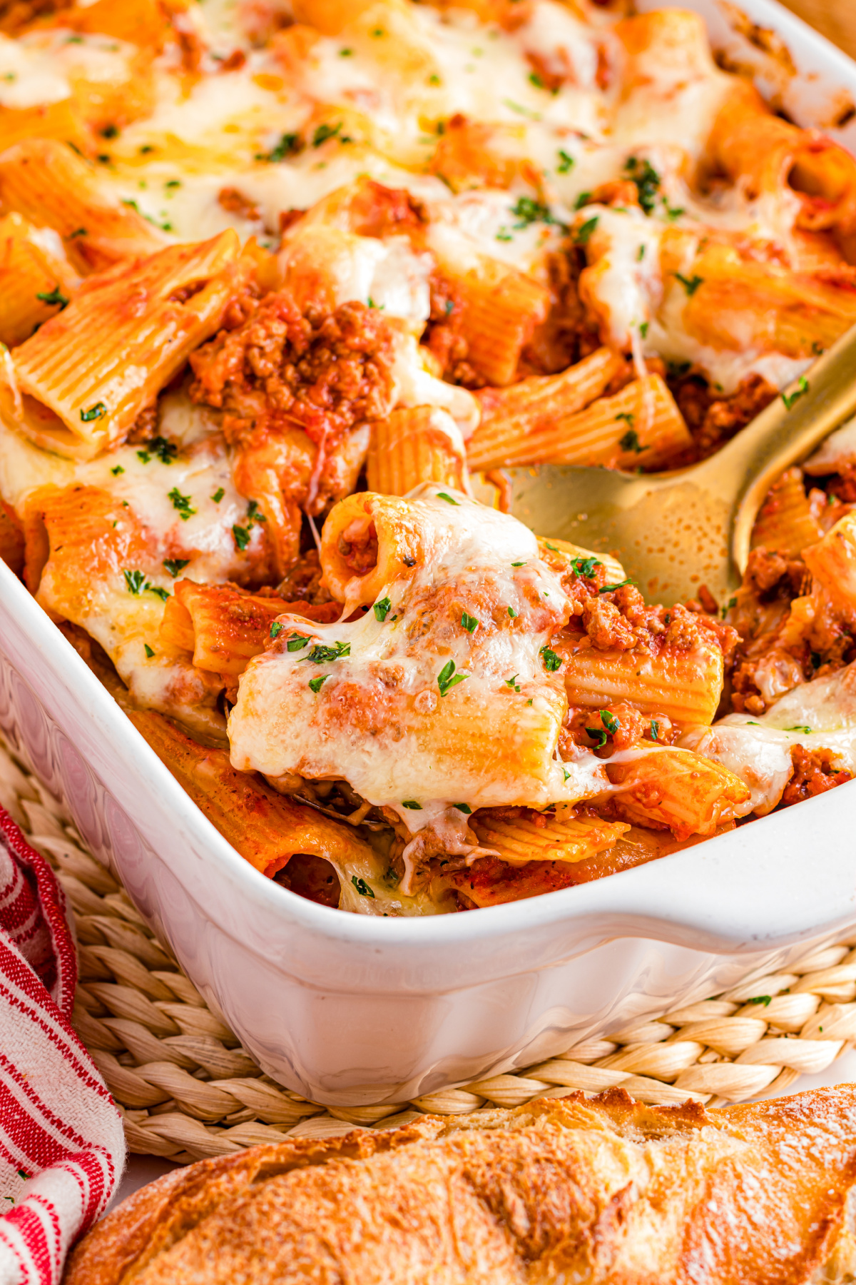 Spoonful of cheesy rigatoni with meat sauce lifted from the baking dish showing melted mozzarella and golden edges