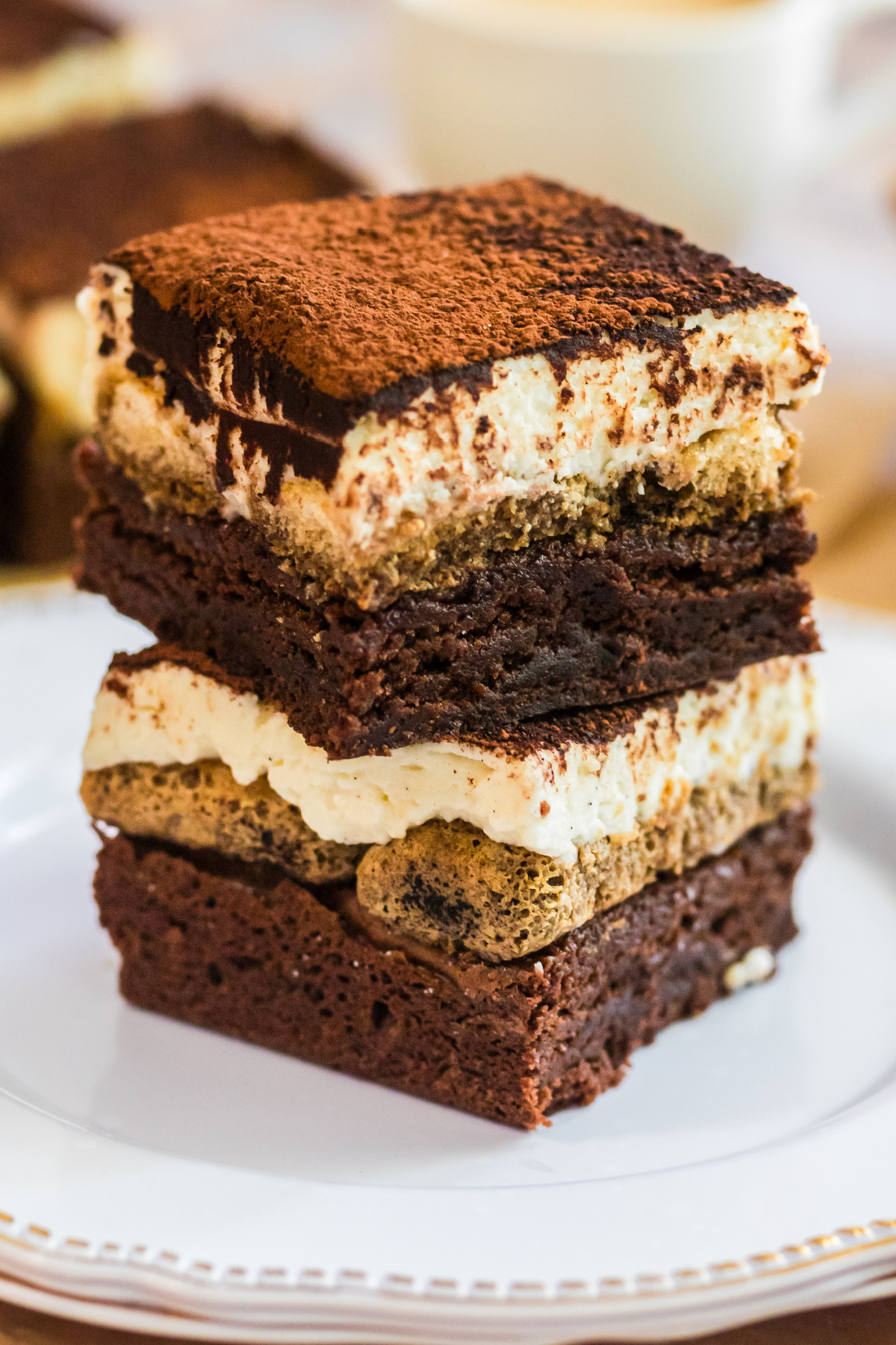 tiramisu brownies stacked dessert with mascarpone and espresso layers. tiramisu brownies stacked on a plate showing espresso-soaked layers, mascarpone cream, and cocoa powder topping.
