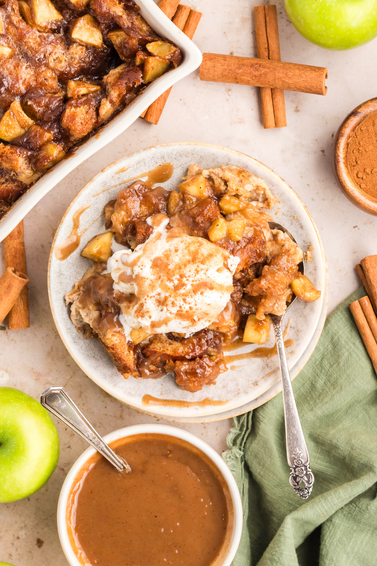 Brioche apple dessert with caramel sauce and ice cream. Overhead view of baked brioche apple dessert topped with ice cream and caramel sauce surrounded by cinnamon sticks and green apples.