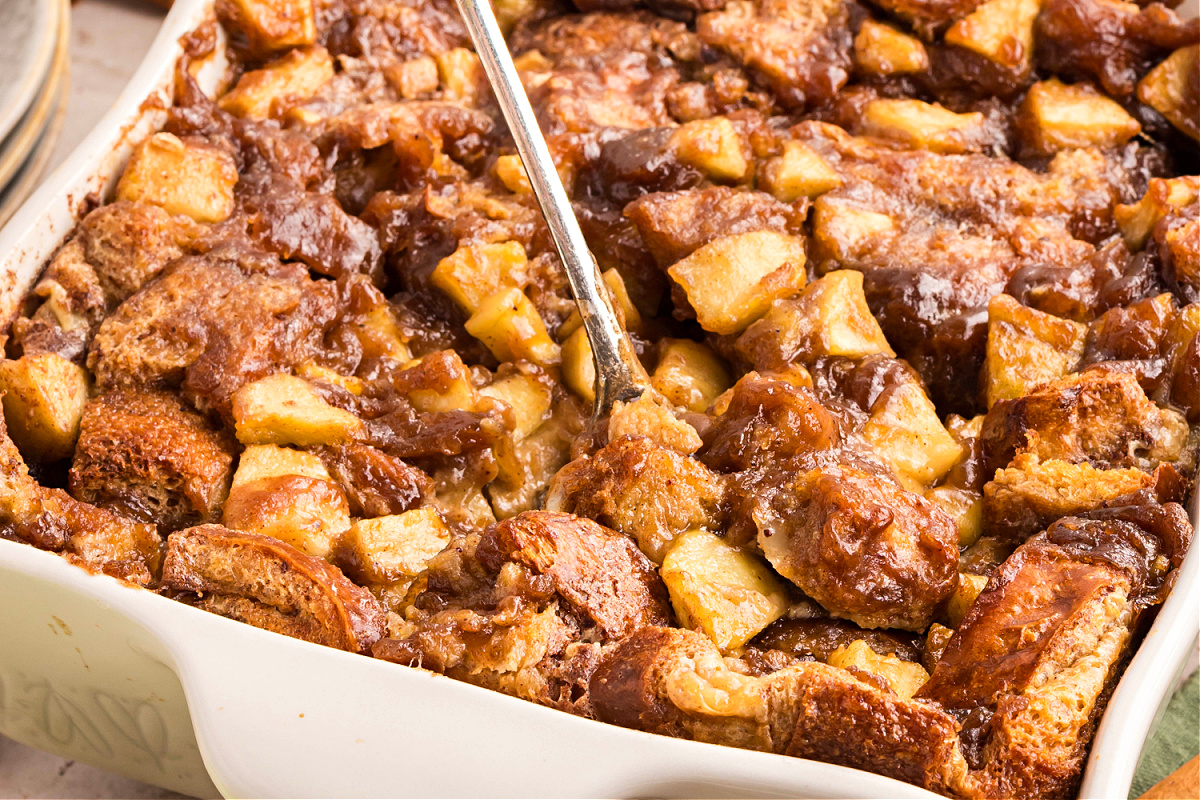 Baked caramel apple bread pudding in a white baking dish. Freshly baked caramel apple bread pudding in a white dish with chunks of brioche and tender apples in caramel sauce.